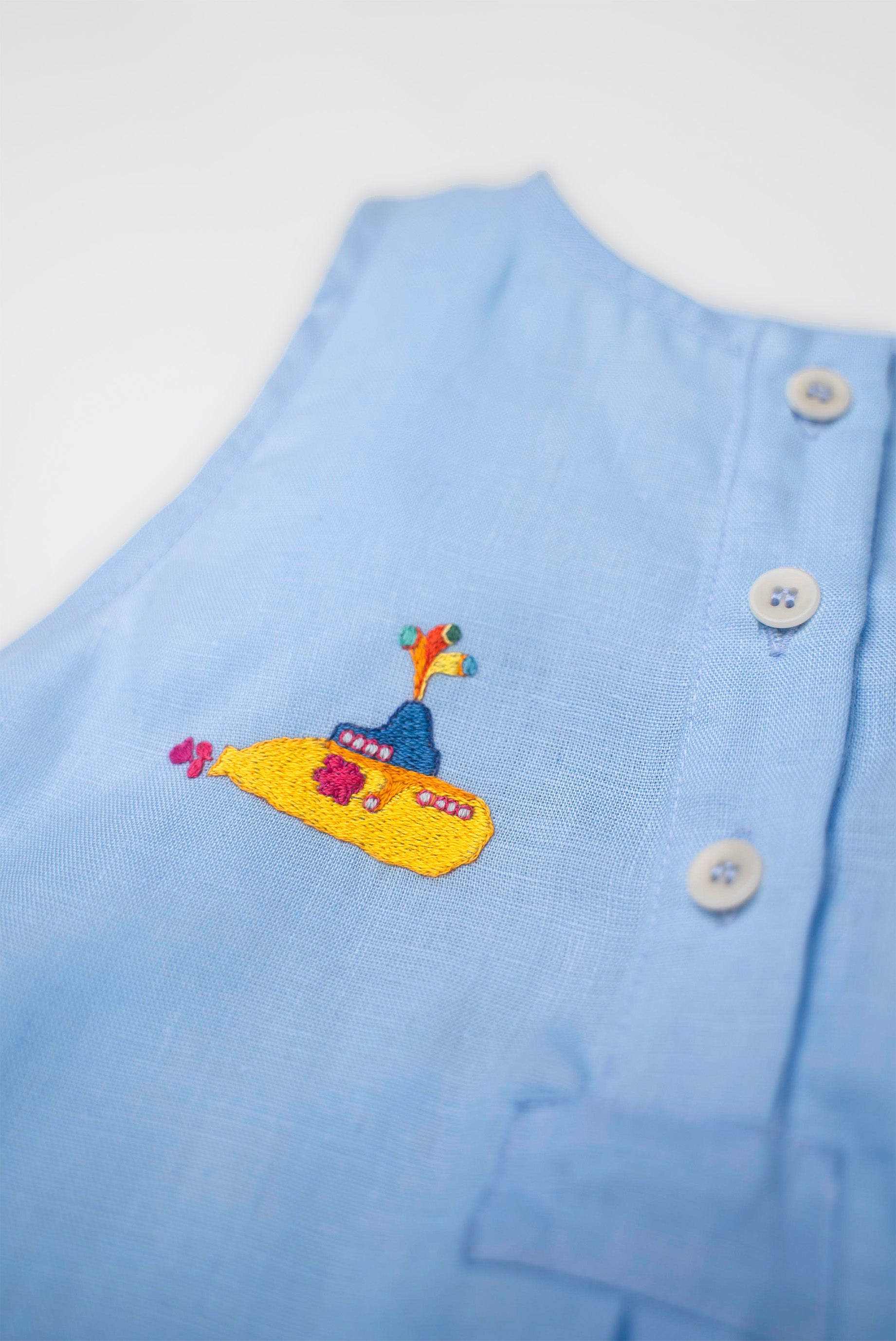 Detalhe do bordado artesanal de submarino amarelo em macaquinho infantil de linho azul, em referência a Yellow Submarine dos Beatles.