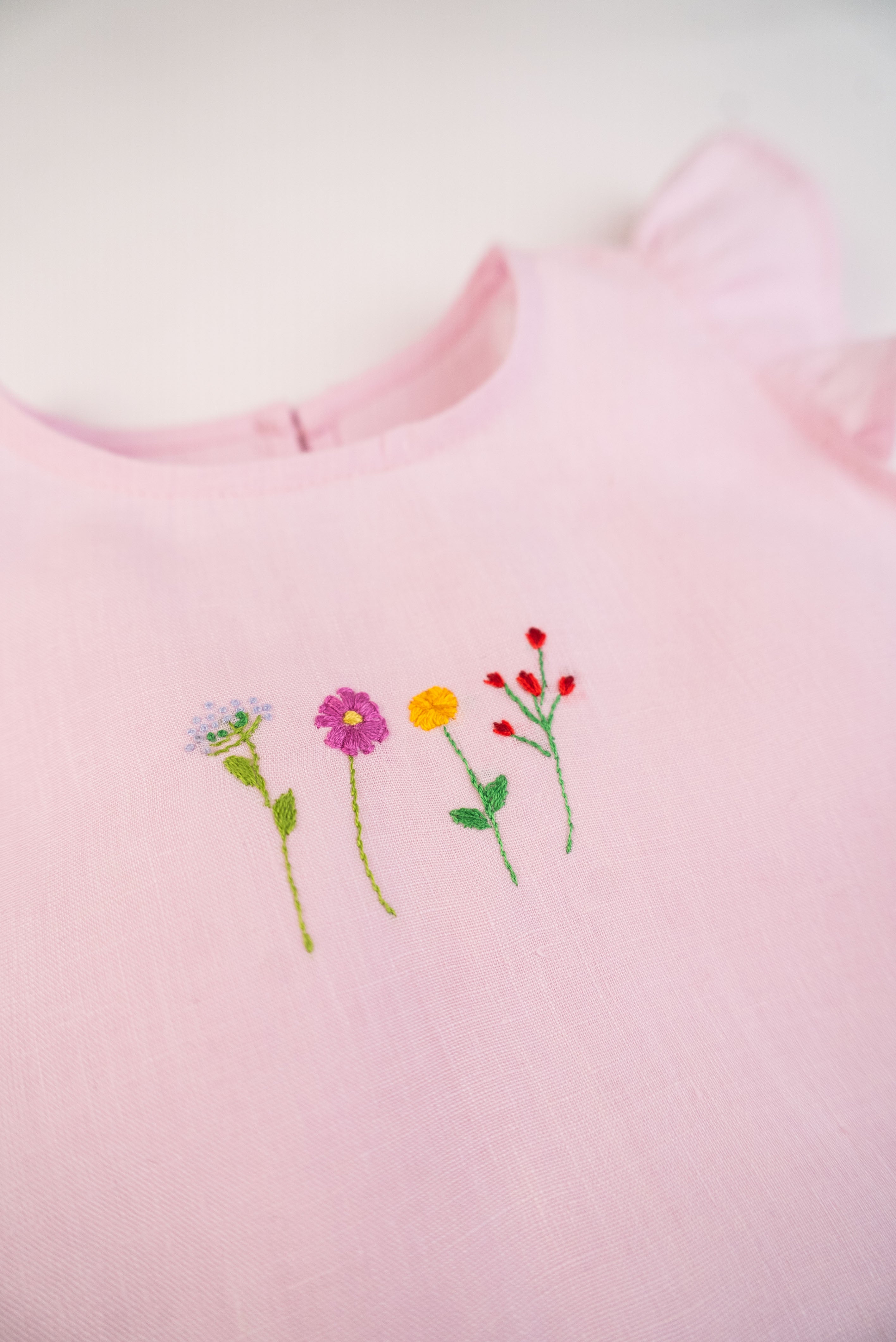 Detalhe do bordado à mão de flores do macaquinho de bebê menina em puro linho rosa.