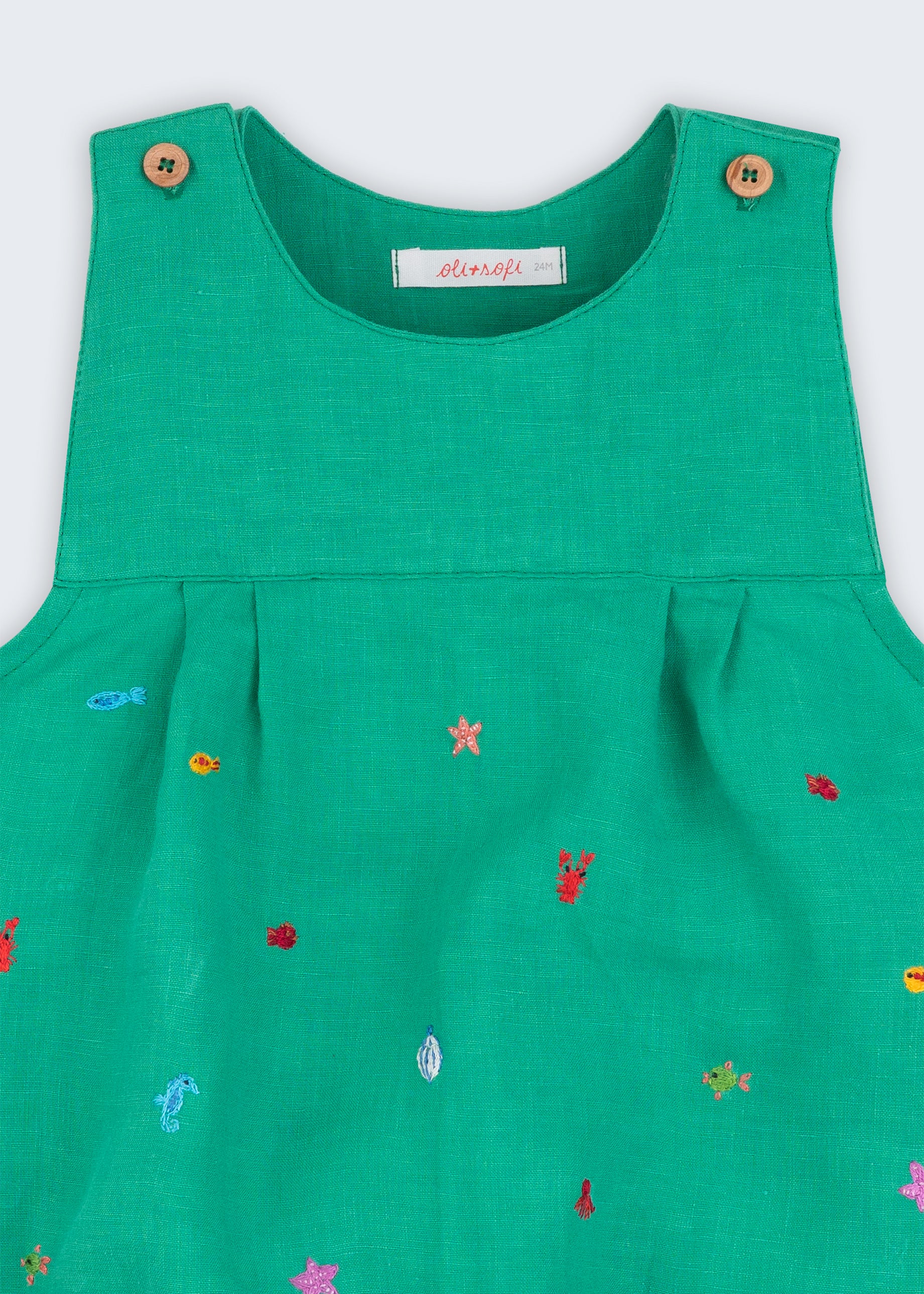 Detalhe do decote com pregas e bordados à mão de peixinhos, conchas e estrelas-do-mar em linho verde-água.