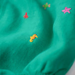 Close dos bordados à mão de cavalo-marinho amarelo e estrela-do-mar rosa nas perninhas do macaquinho de bebê.