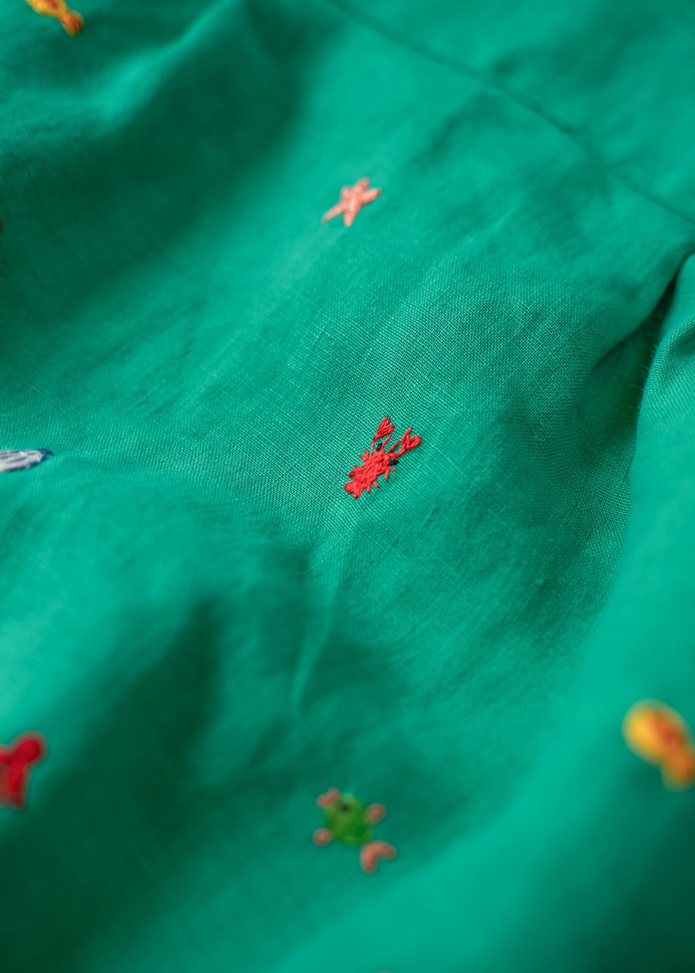 Close do bordado à mão de lagosta vermelha no macaquinho de linho verde-água.