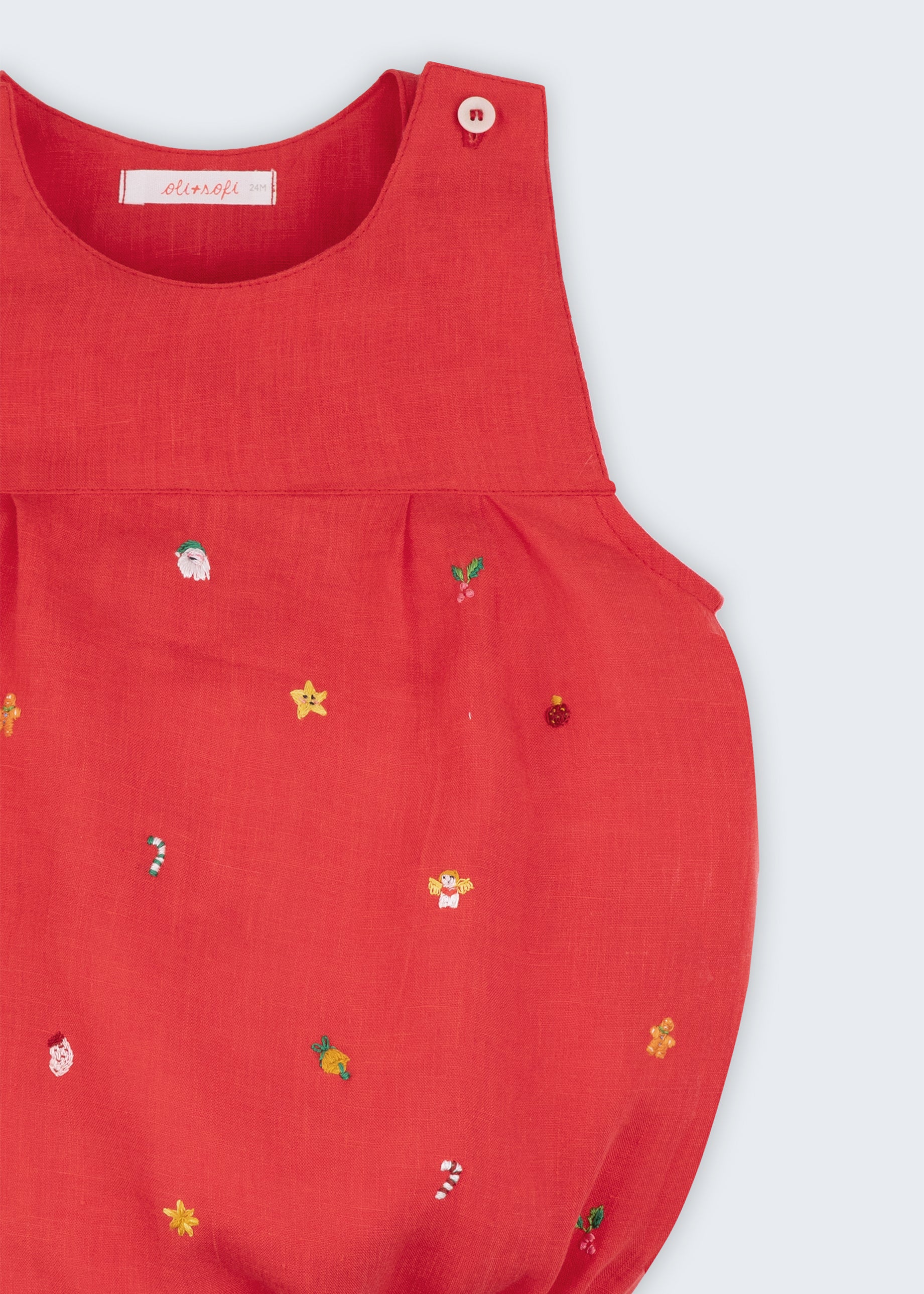 Detalhe dos bordados manuais natalinos em macaquinho de bebê vermelho de linho.