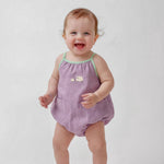 Bebê menina vestindo macaquinho infantil lilás com viés verde e bordado à mão de ovelhinhas.