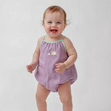 Bebê menina vestindo macaquinho infantil lilás com viés verde e bordado à mão de ovelhinhas.