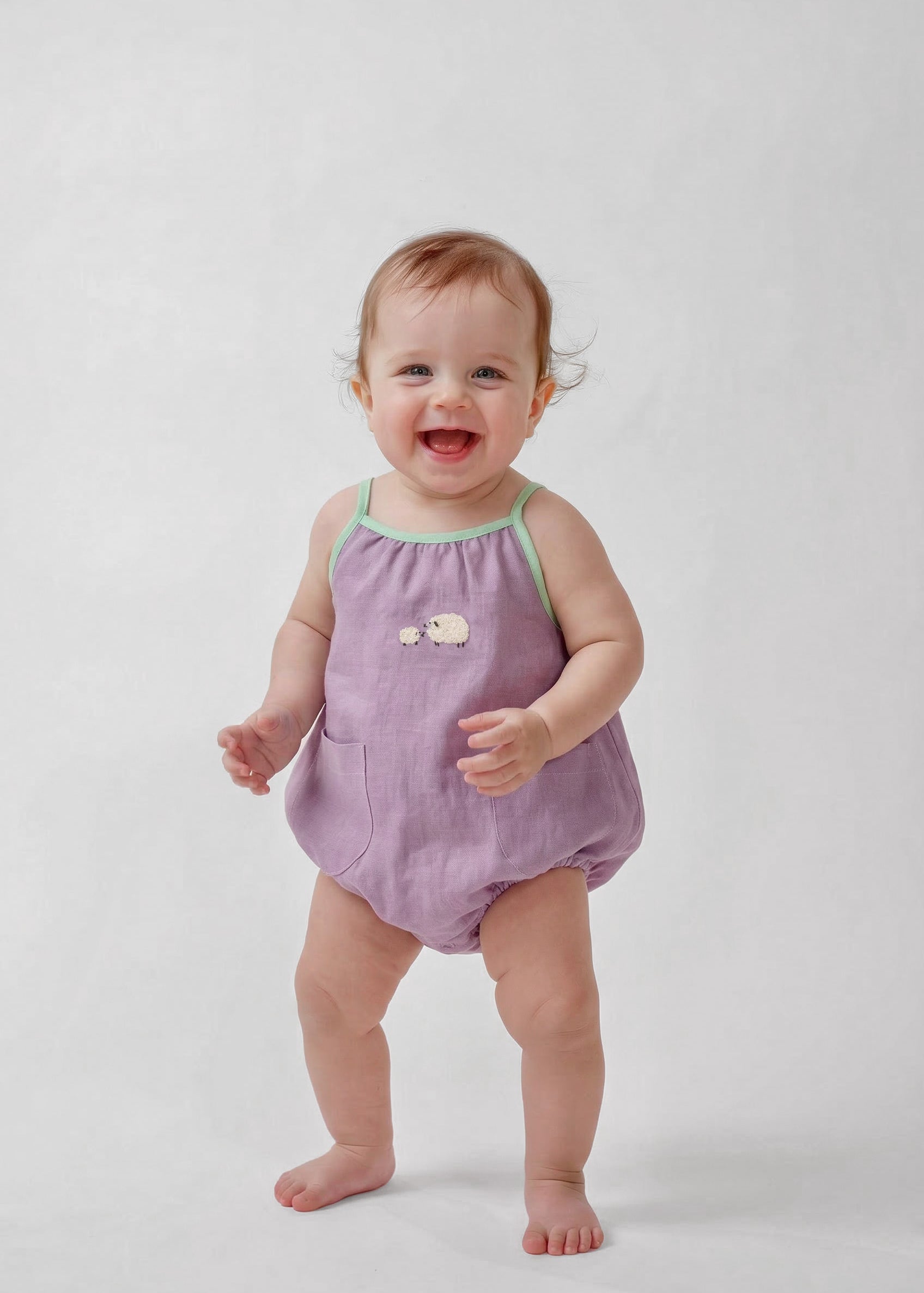 Bebê menina vestindo macaquinho infantil lilás com viés verde e bordado à mão de ovelhinhas.