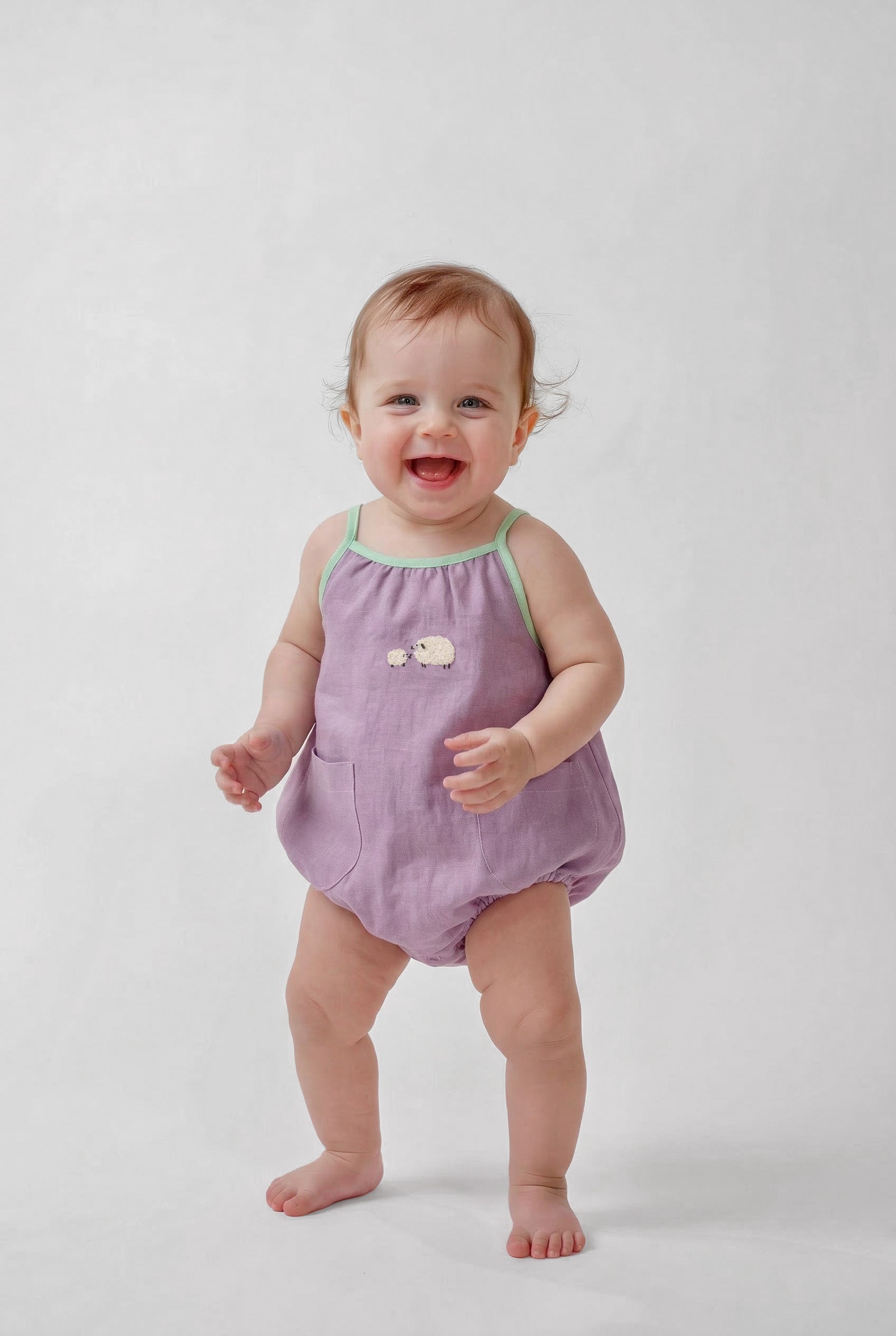 Bebê menina vestindo macaquinho infantil lilás com viés verde e bordado à mão de ovelhinhas.