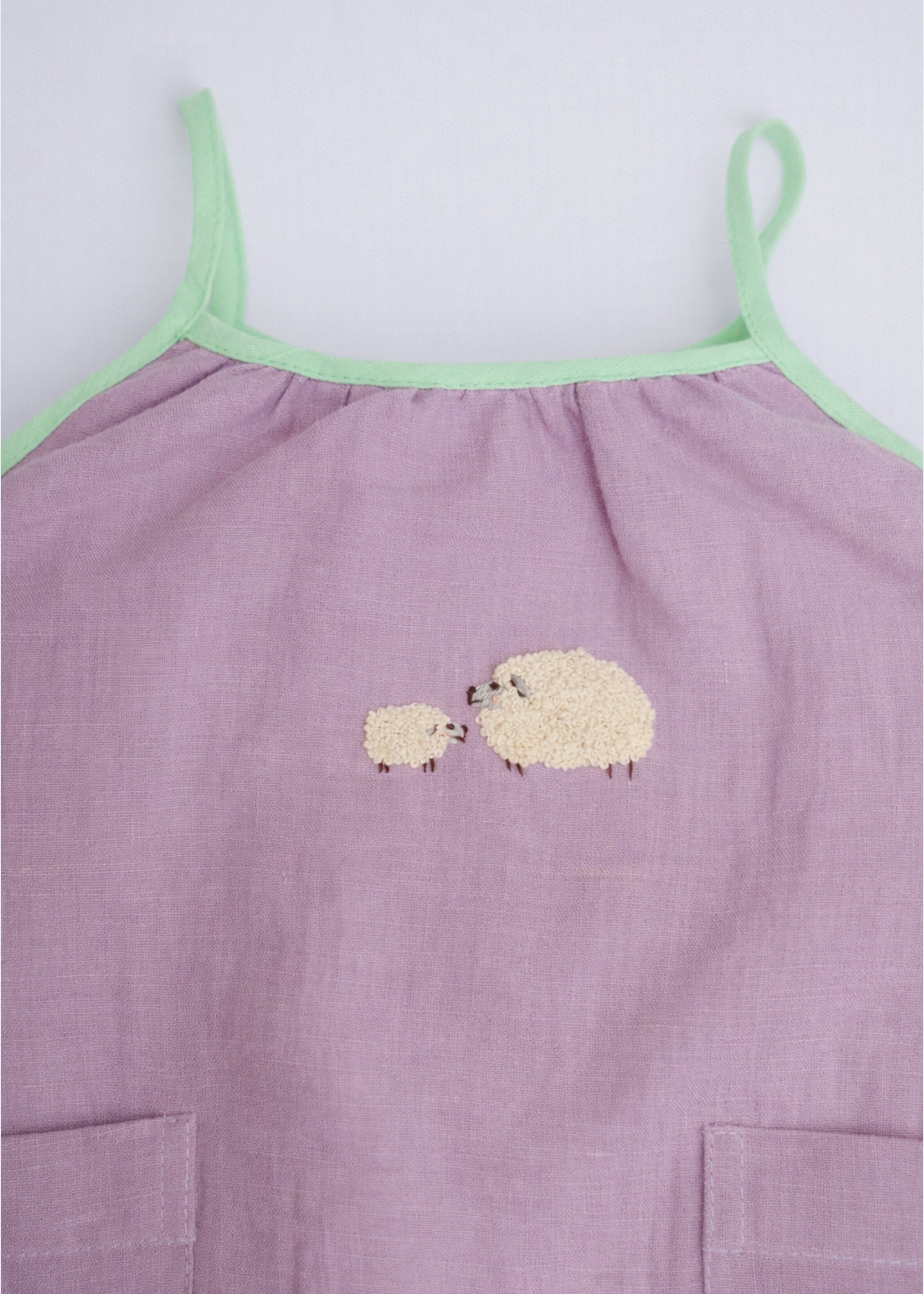 Detalhe do bordado à mão de duas ovelhinhas em macaquinho infantil lilás para bebê menina.