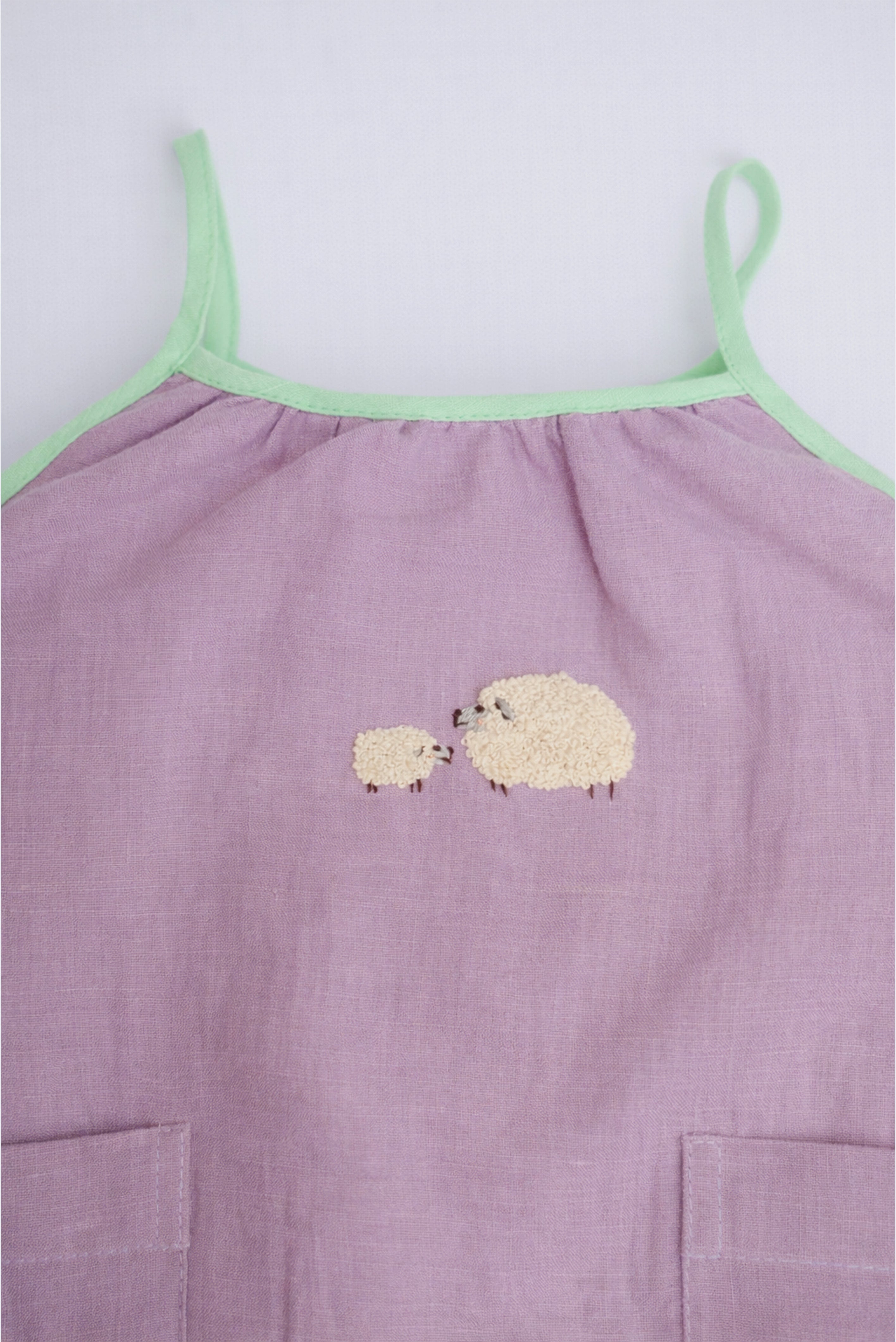 Detalhe do bordado à mão de duas ovelhinhas em macaquinho infantil lilás para bebê menina.