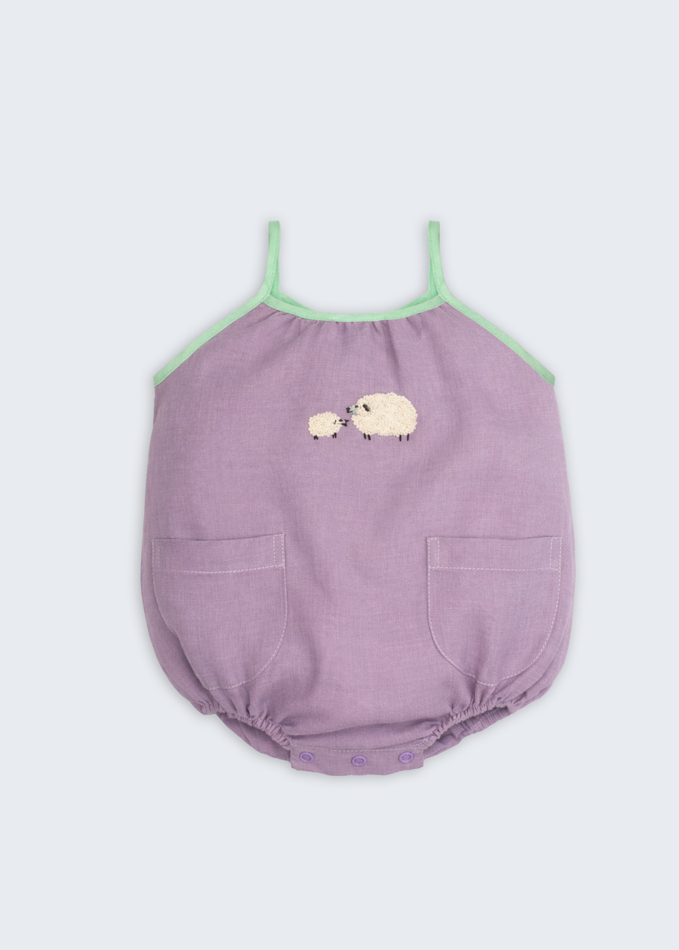 Macaquinho infantil de menina em linho lilás com viés verde, bolsos frontais e bordado artesanal de ovelhas.