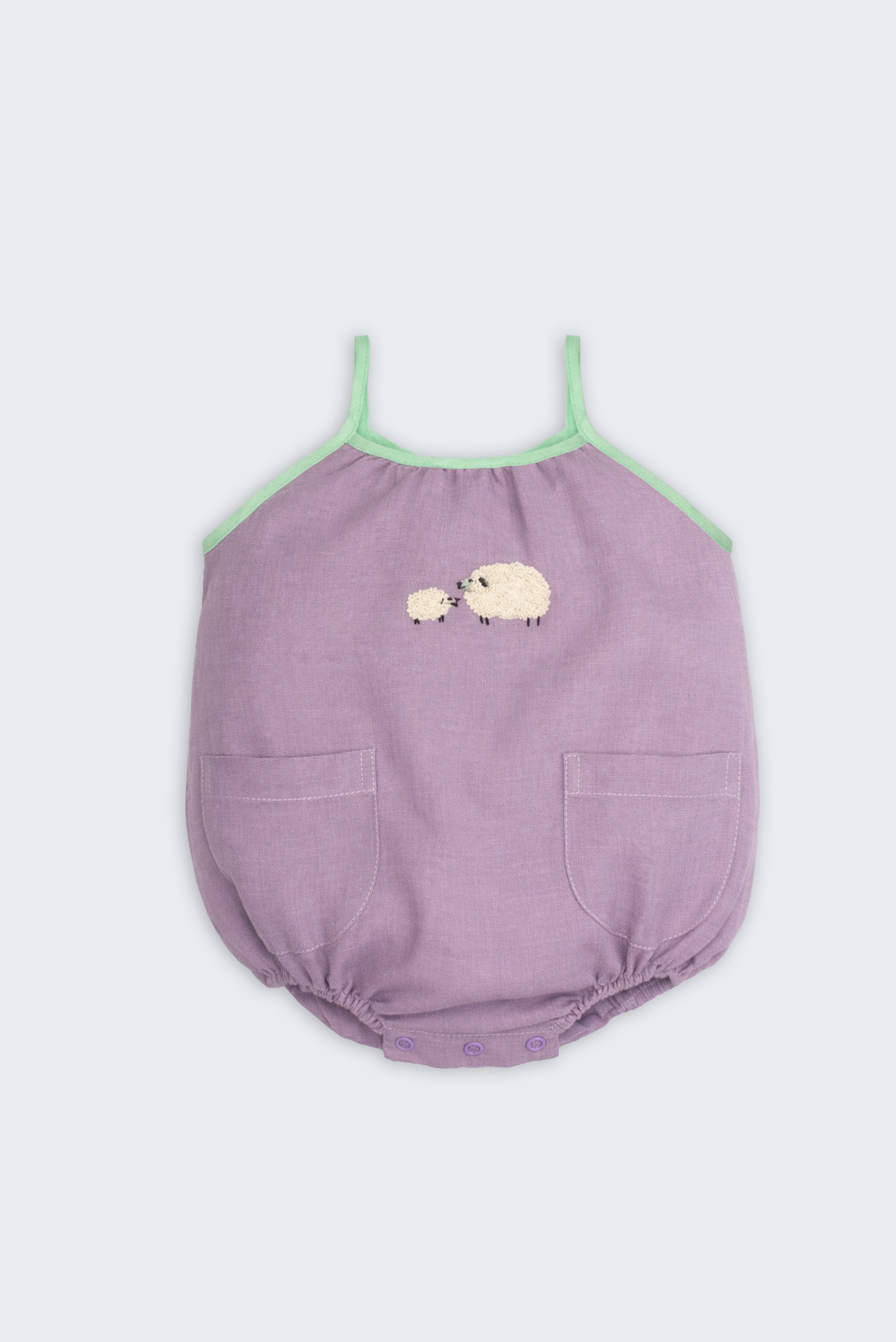 Macaquinho infantil de menina em linho lilás com viés verde, bolsos frontais e bordado artesanal de ovelhas.