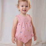 Bebê menina vestindo macaquinho infantil de linho rosa com flores bordadas à mão.