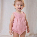 Bebê menina vestindo macaquinho infantil de linho rosa com flores bordadas à mão.