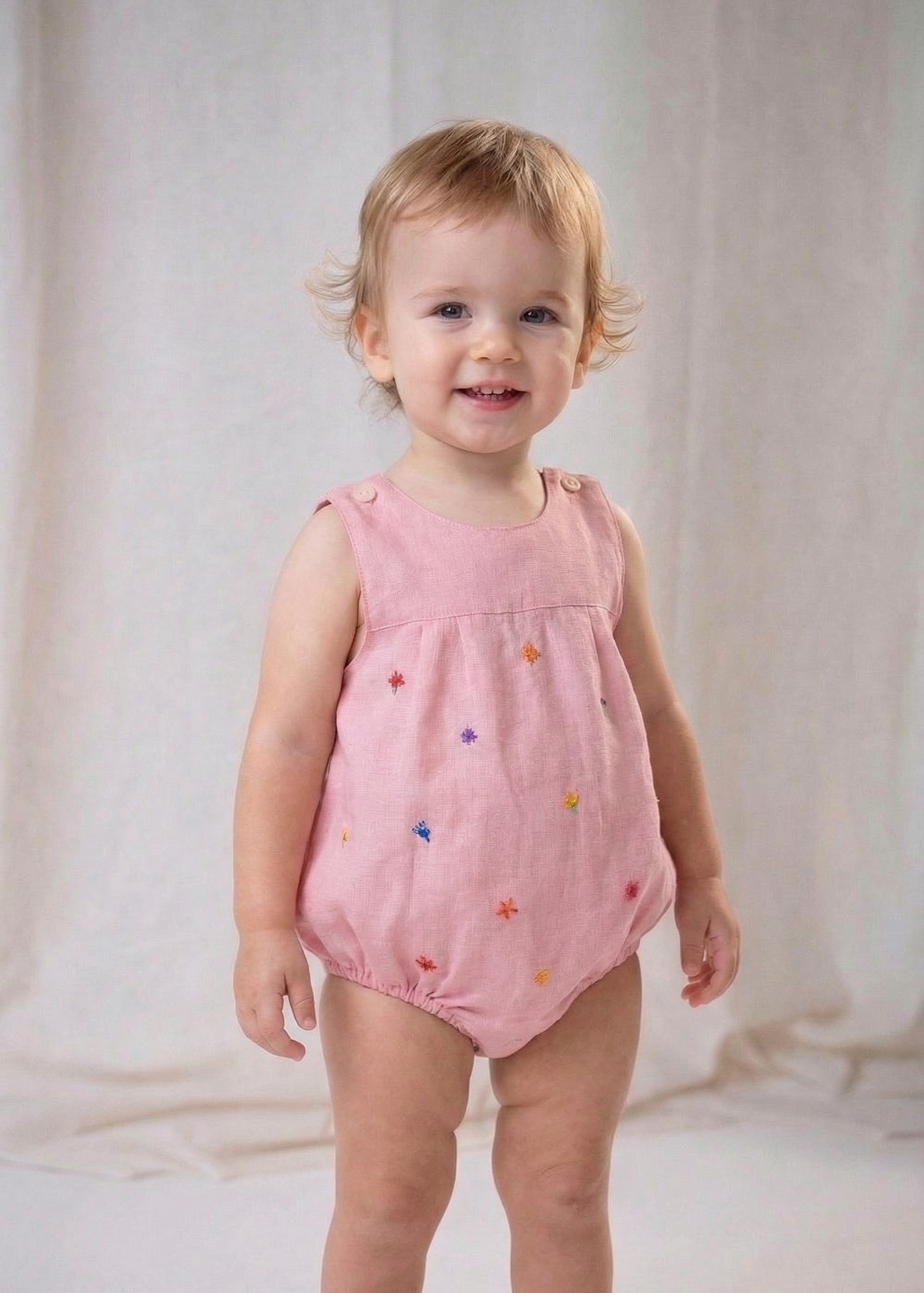 Bebê menina vestindo macaquinho infantil de linho rosa com flores bordadas à mão.