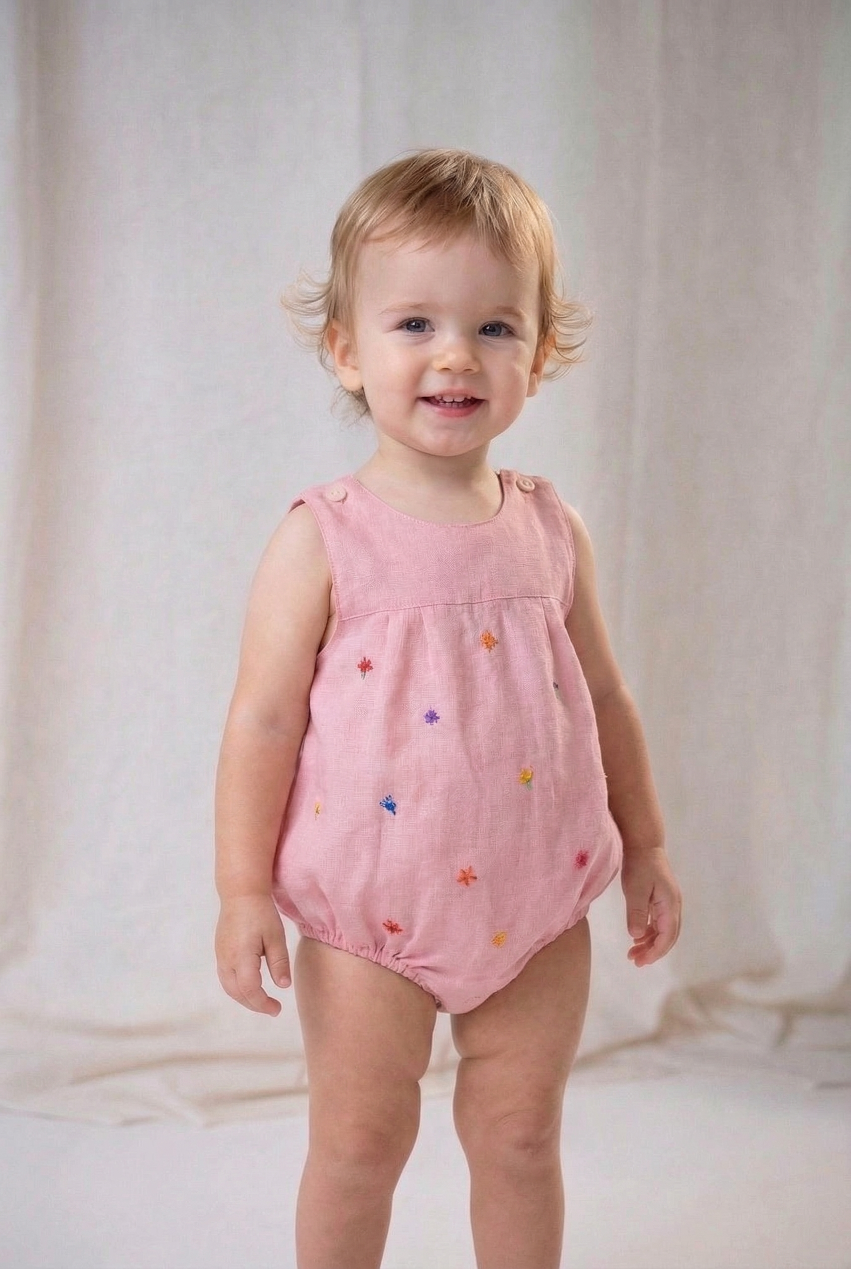 Bebê menina vestindo macaquinho infantil de linho rosa com flores bordadas à mão.