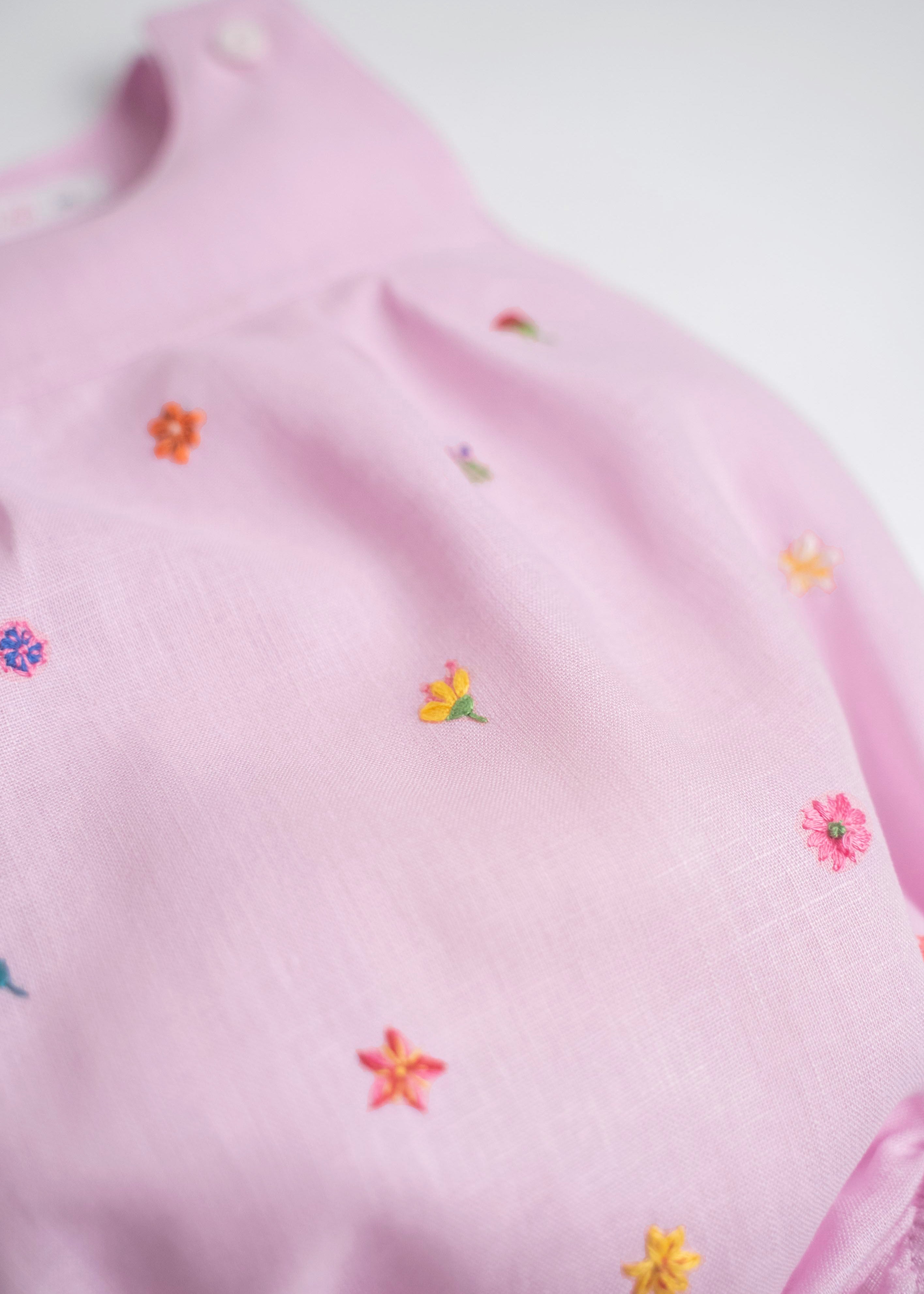 Detalhe de flores bordadas à mão em macaquinho infantil de linho rosa.