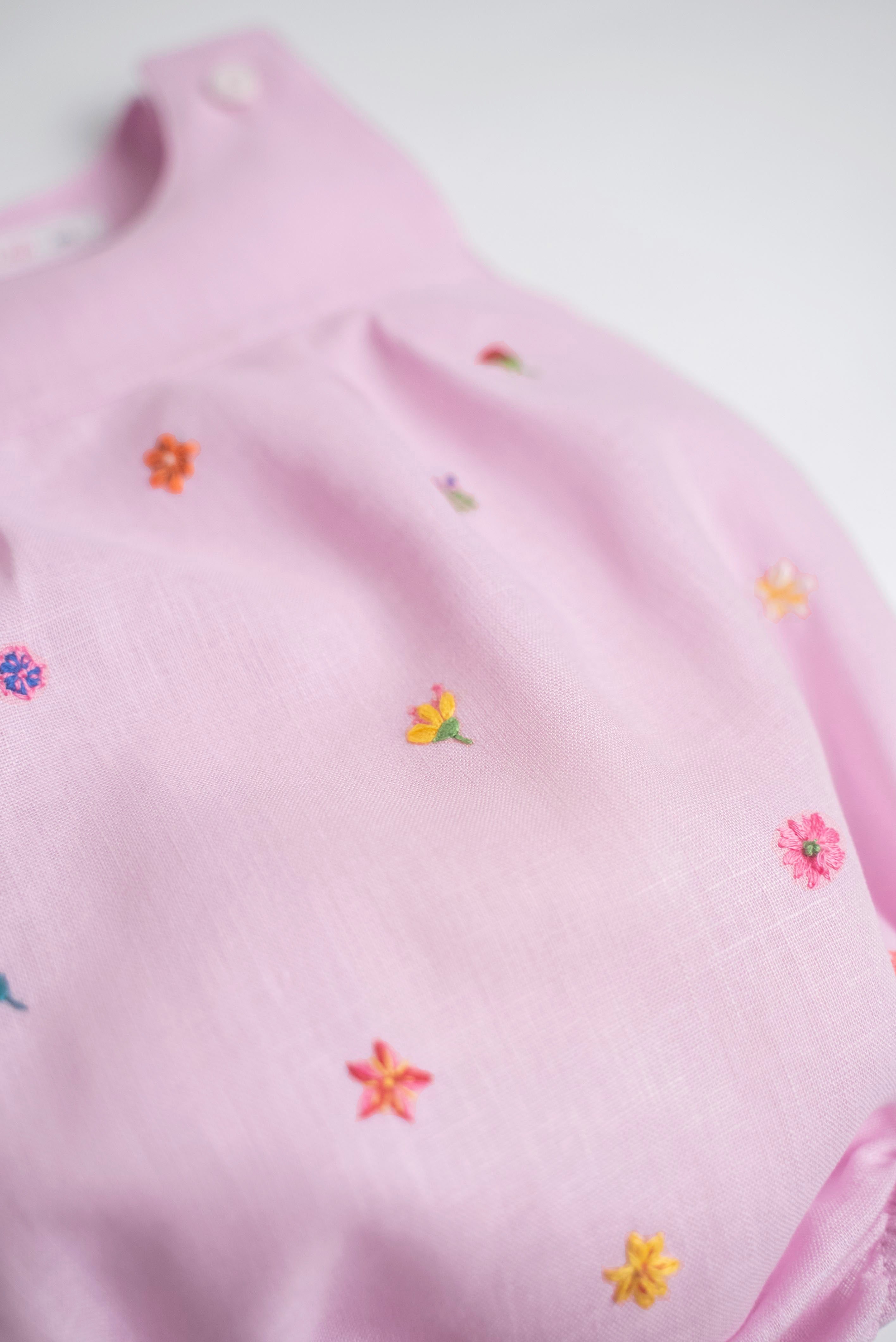 Detalhe de flores bordadas à mão em macaquinho infantil de linho rosa.
