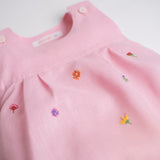 Detalhe de flores bordadas à mão em macaquinho infantil de linho rosa.