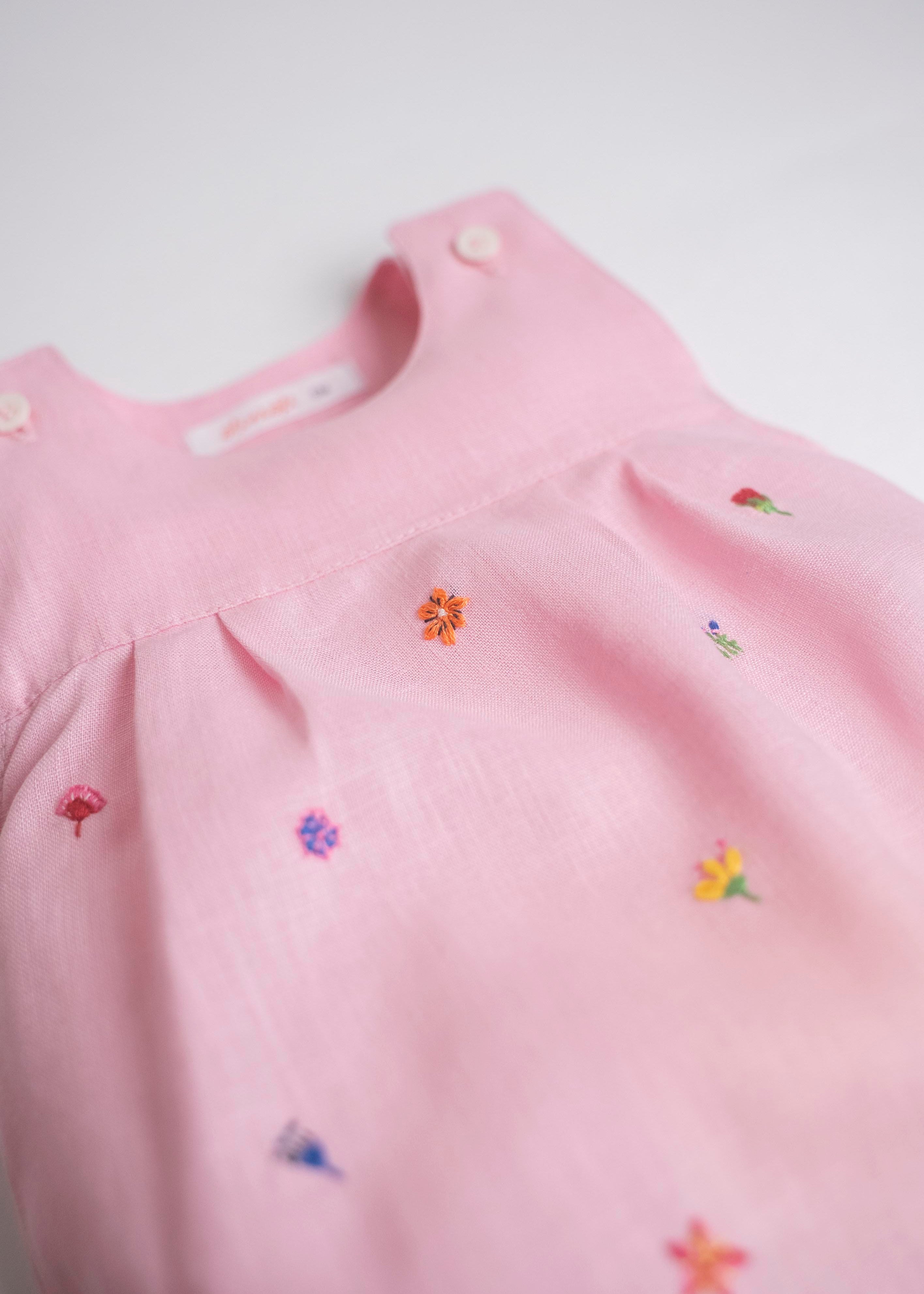 Detalhe de flores bordadas à mão em macaquinho infantil de linho rosa.
