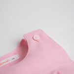 Detalhe do botão no ombro do macaquinho infantil de menina em linho rosa.