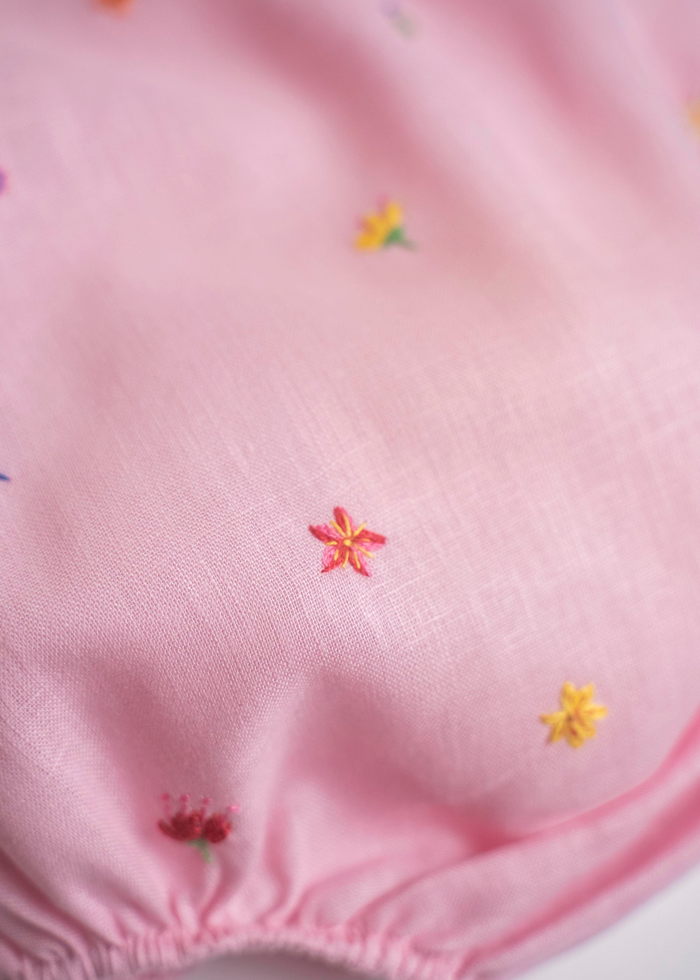 Flor bordada à mão em macaquinho infantil de linho rosa para bebê.