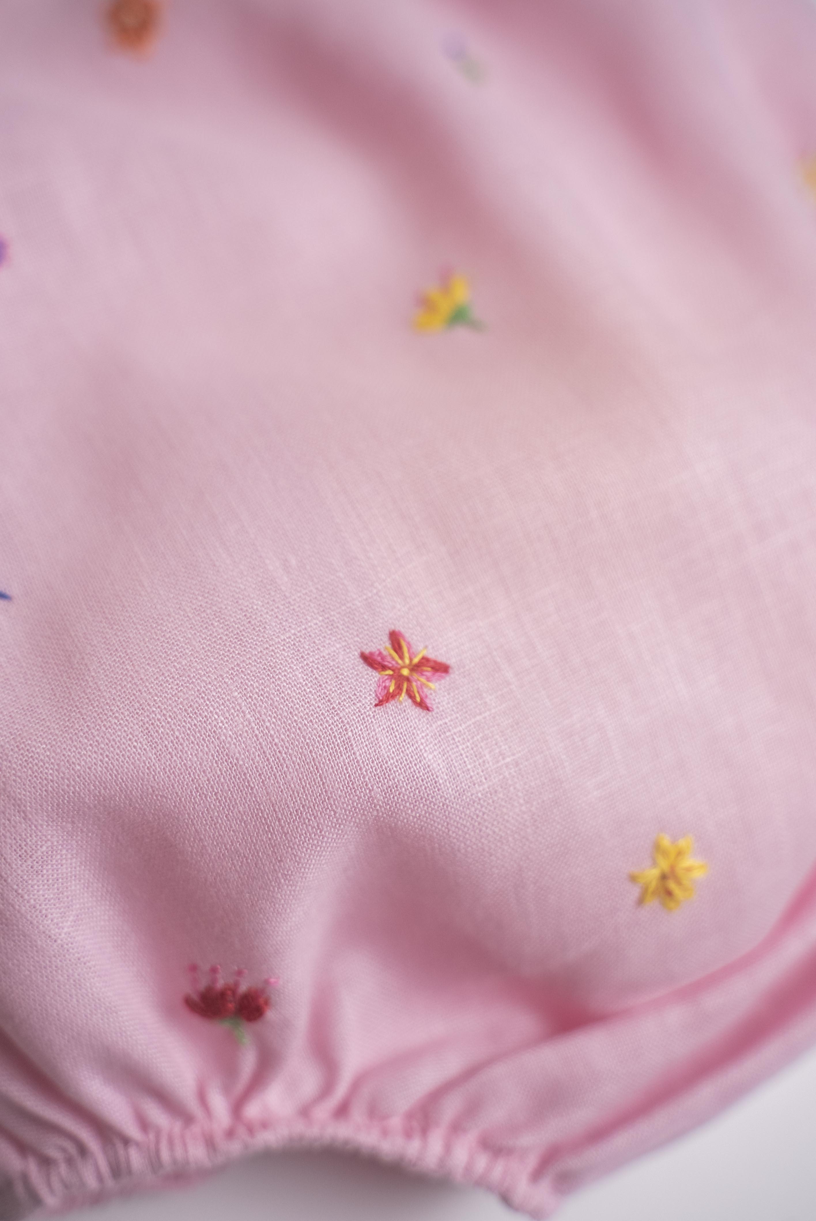 Flor bordada à mão em macaquinho infantil de linho rosa para bebê.