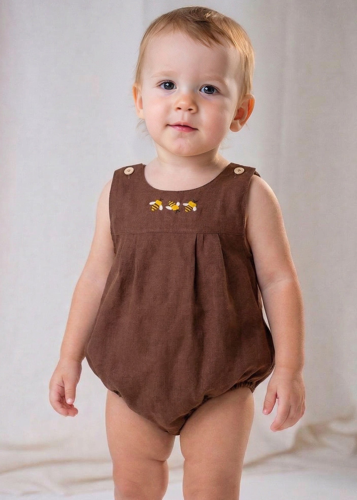 Bebê menino usando macaquinho infantil em linho marrom com bordado à mão de abelhas, também conhecido como romper.