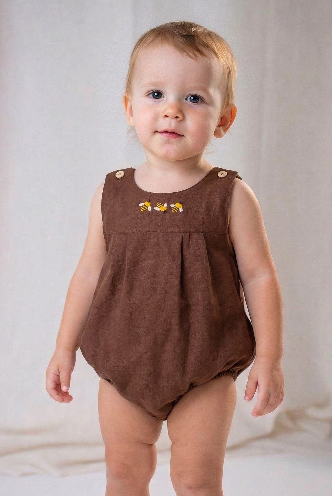 Bebê menino usando macaquinho infantil em linho marrom com bordado à mão de abelhas, também conhecido como romper.
