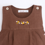 Macaquinho de bebê em linho marrom com três abelhas bordadas à mão no peito, visto em detalhe.