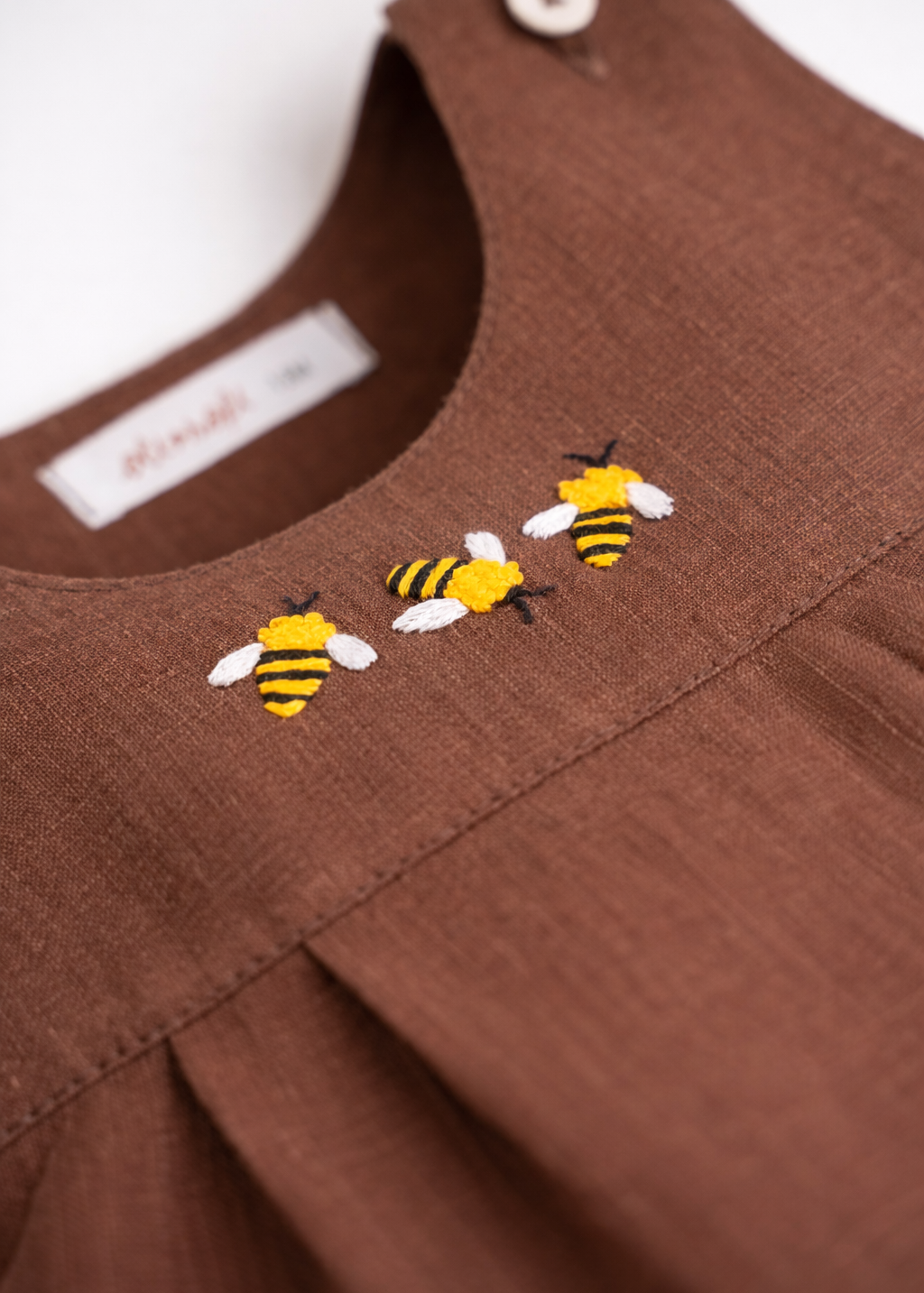 Detalhe do bordado artesanal de abelha em macaquinho infantil de linho marrom para bebê.