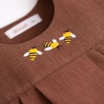 Detalhe do bordado artesanal de abelha em macaquinho infantil de linho marrom para bebê.