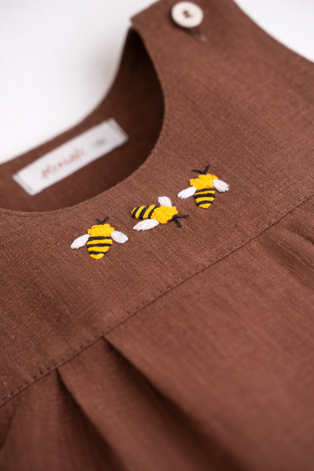Detalhe do bordado artesanal de abelha em macaquinho infantil de linho marrom para bebê.