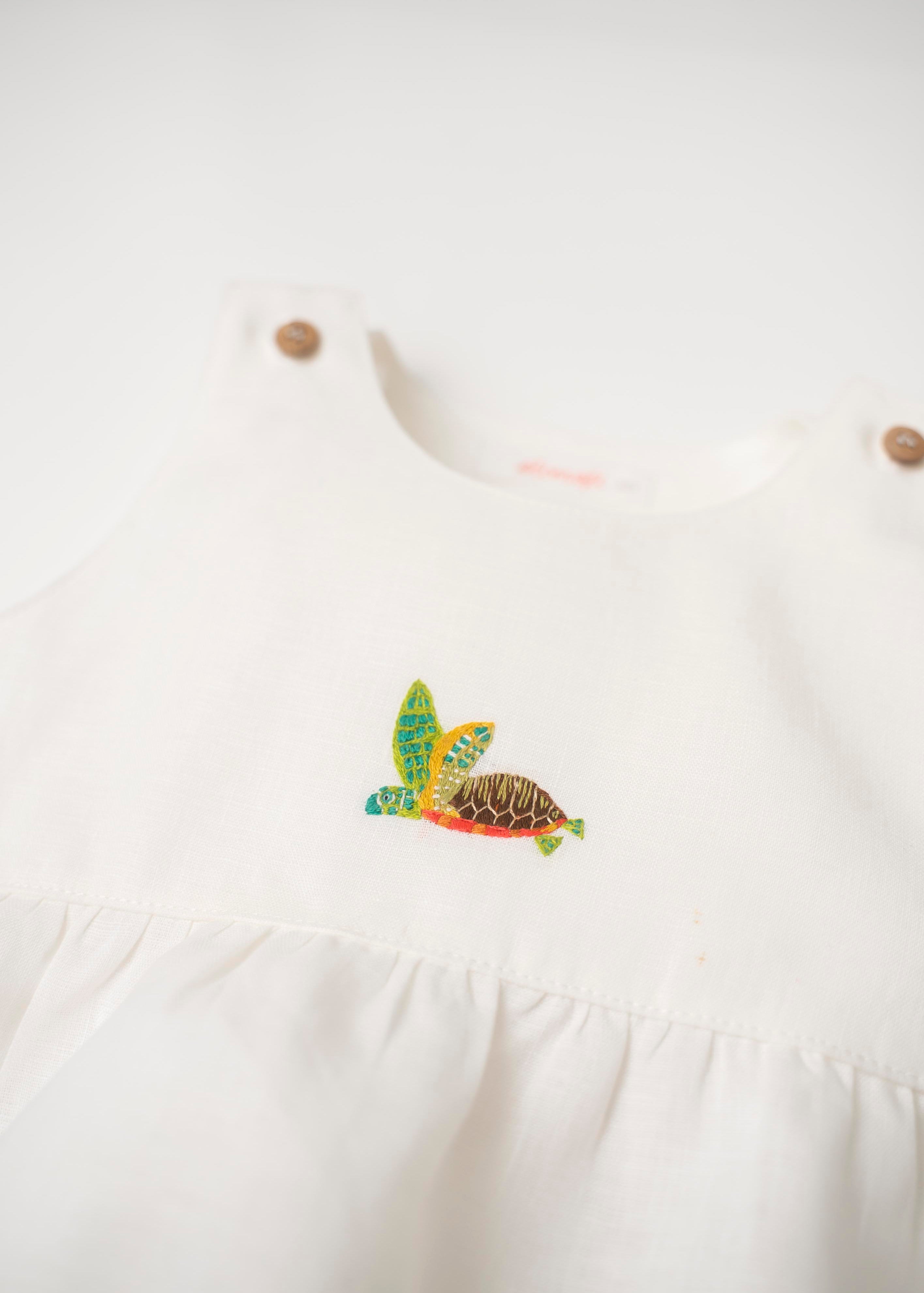 Detalhe de macaquinho de bebê em linho branco com bordado à mão de tartaruga marinha no peito, para meninos e meninas.