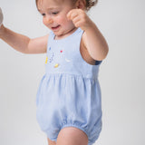 Bebê usando macaquinho de linho azul claro com modelagem balonê e bordado artesanal de sol, lua e estrelas.