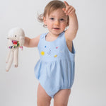 Bebê usando macaquinho de linho azul claro com modelagem balonê e bordado artesanal de sol, lua e estrelas.