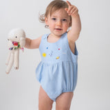 Bebê usando macaquinho de linho azul claro com modelagem balonê e bordado artesanal de sol, lua e estrelas.