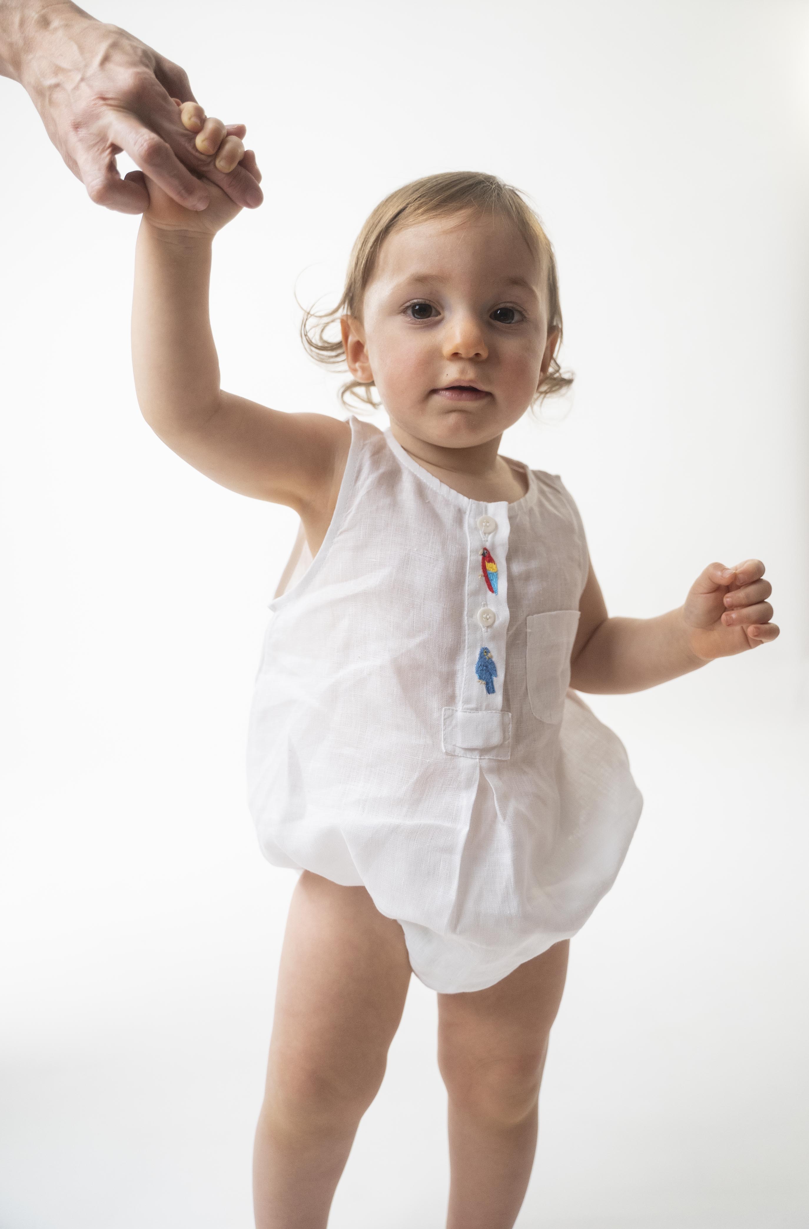 Bebê usando Macaquinho Valen de linho branco com araras bordadas à mão e modelagem soltinha.