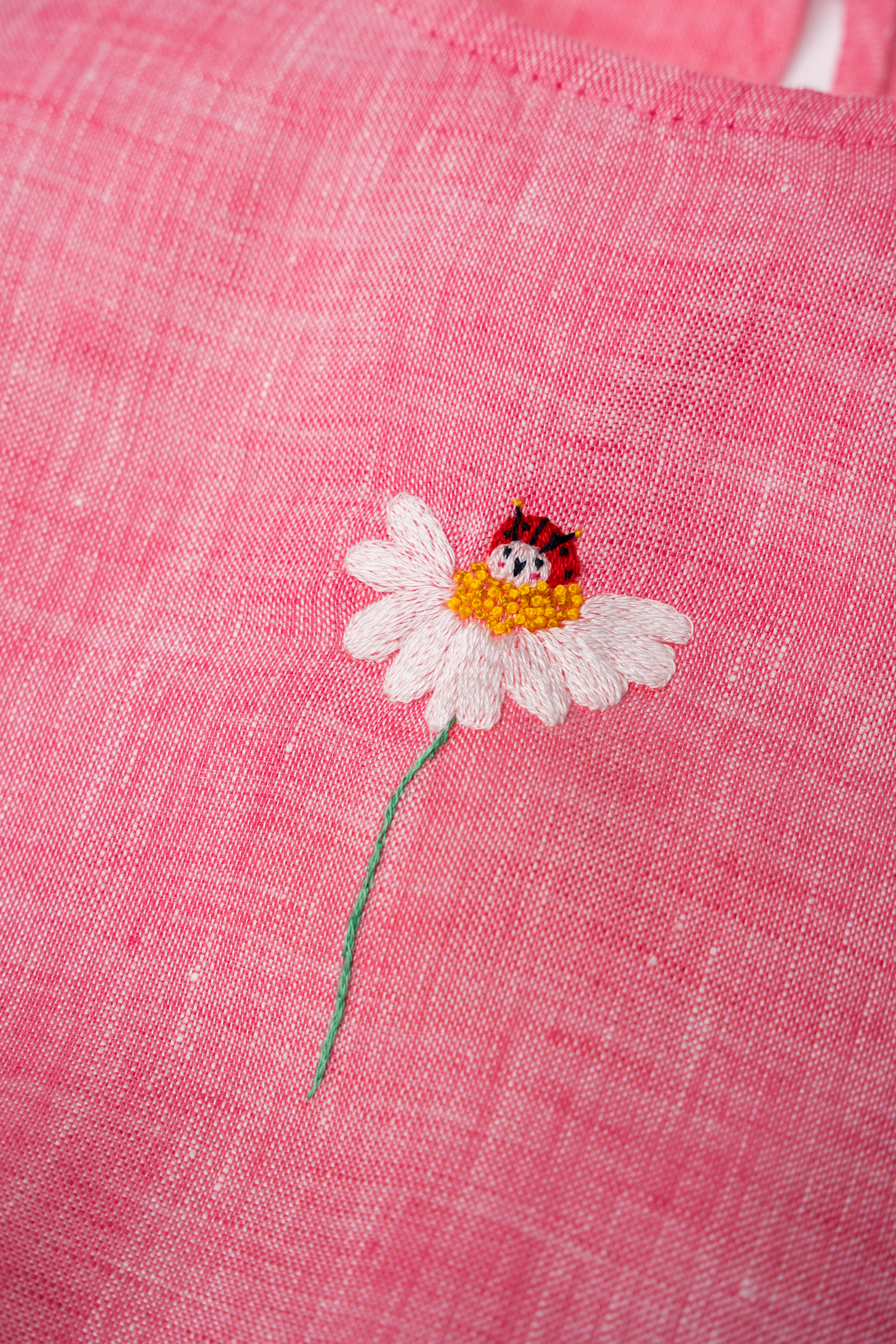Detalhe de bordado de flor com joaninha do Macaquinho Clara em linho fio tinto rosa