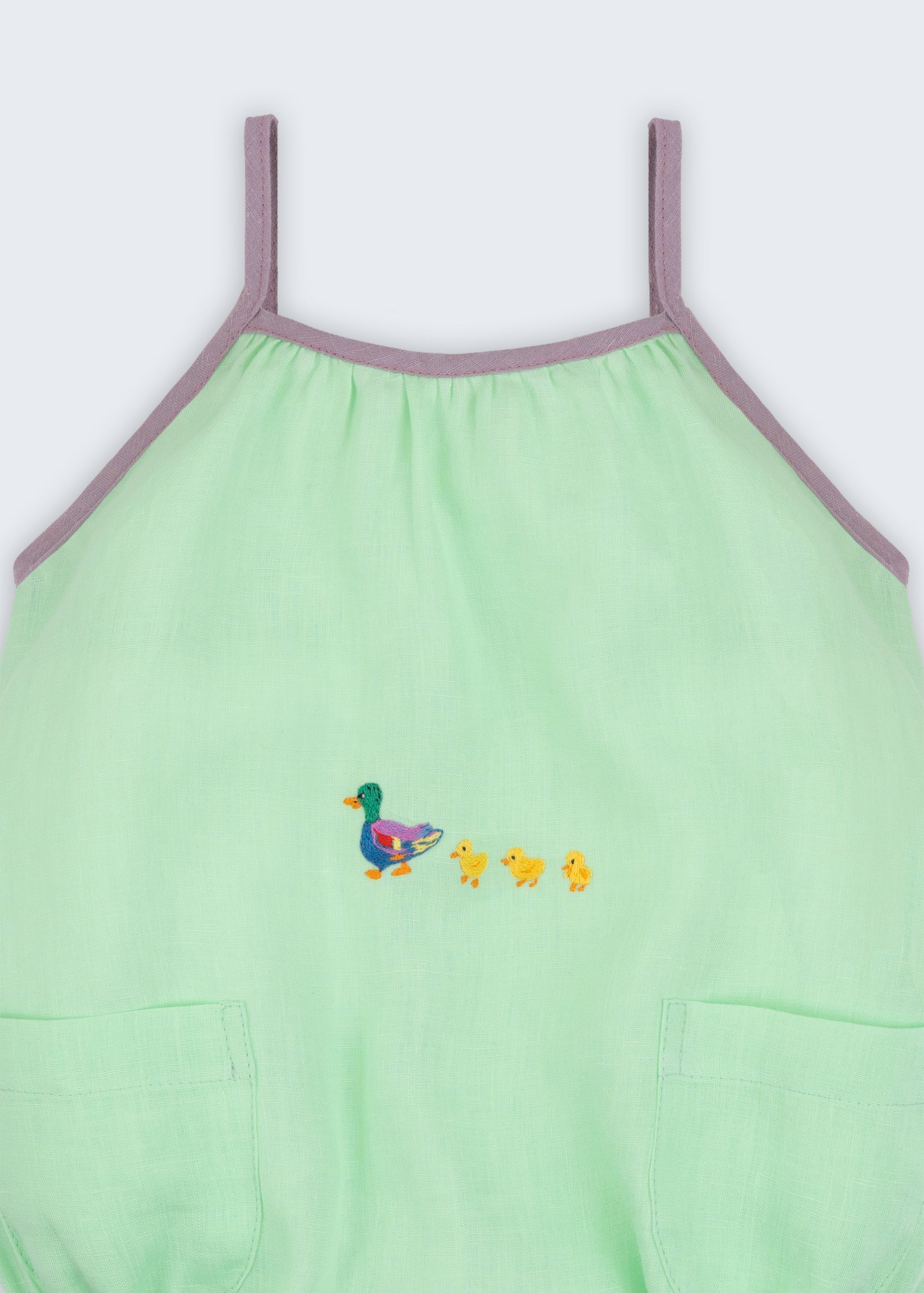 Detalhe do macaquinho em linho verde menta com alças finas e viés lilás; patinhos bordados ao centro.