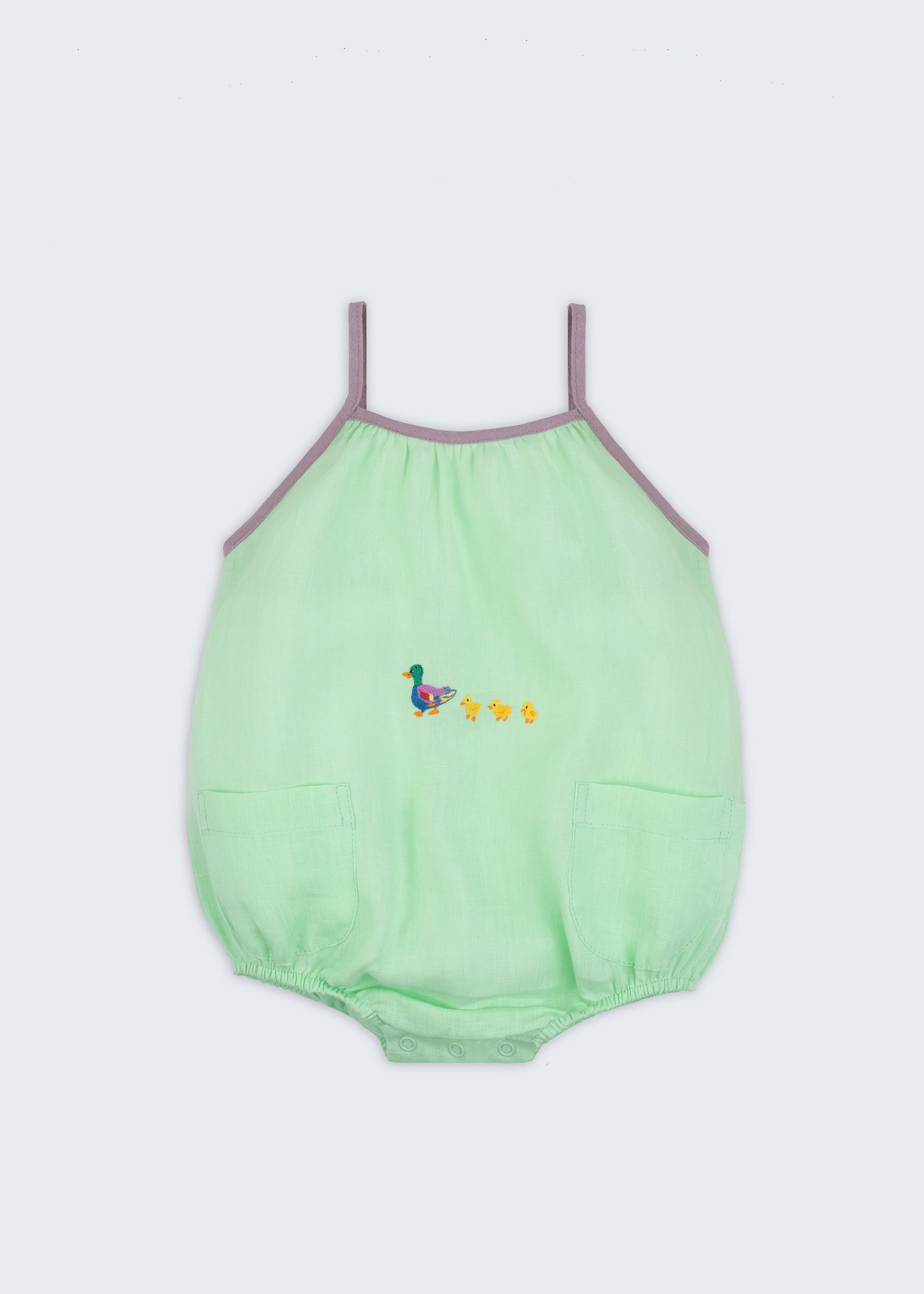 Macaquinho infantil em linho verde menta com alças finas na cor lilás, bolsos frontais e patinhos bordados à mão na altura da barriga, para bebês meninos e meninas.