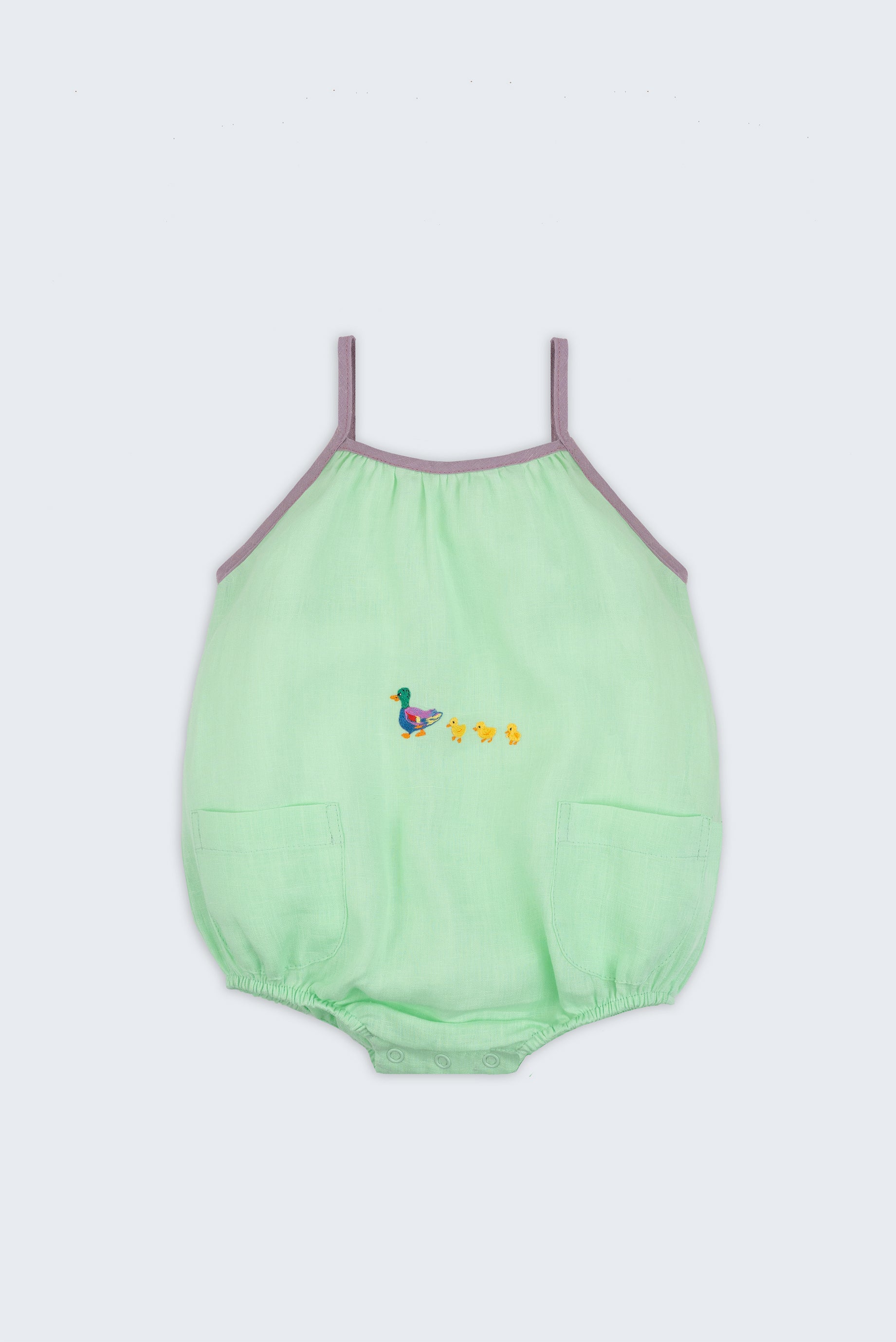 Macaquinho infantil em linho verde menta com alças finas na cor lilás, bolsos frontais e patinhos bordados à mão na altura da barriga, para bebês meninos e meninas.