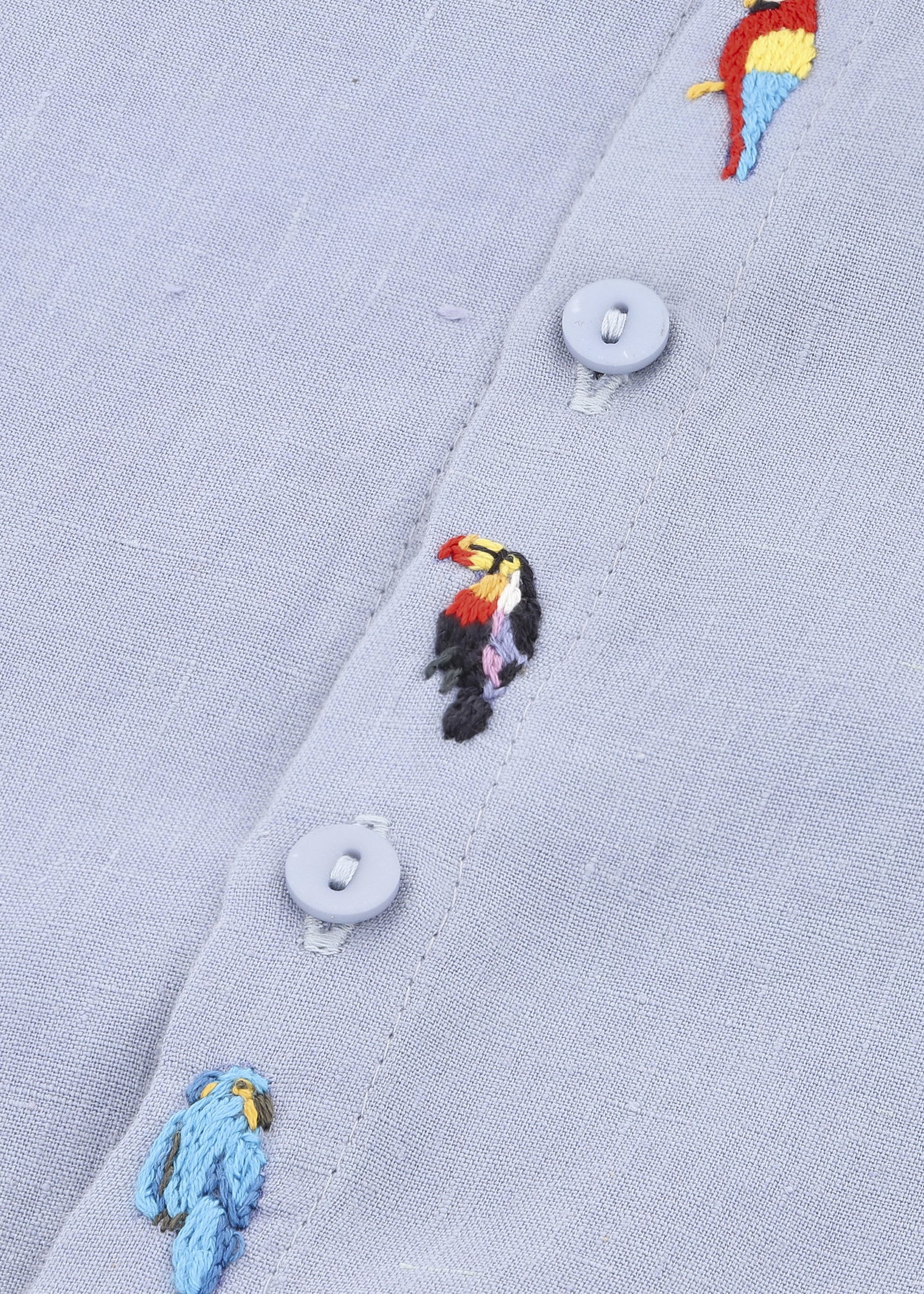 Detalhe dos bordados à mão de tucano e arara em macaquinho infantil de linho azul claro