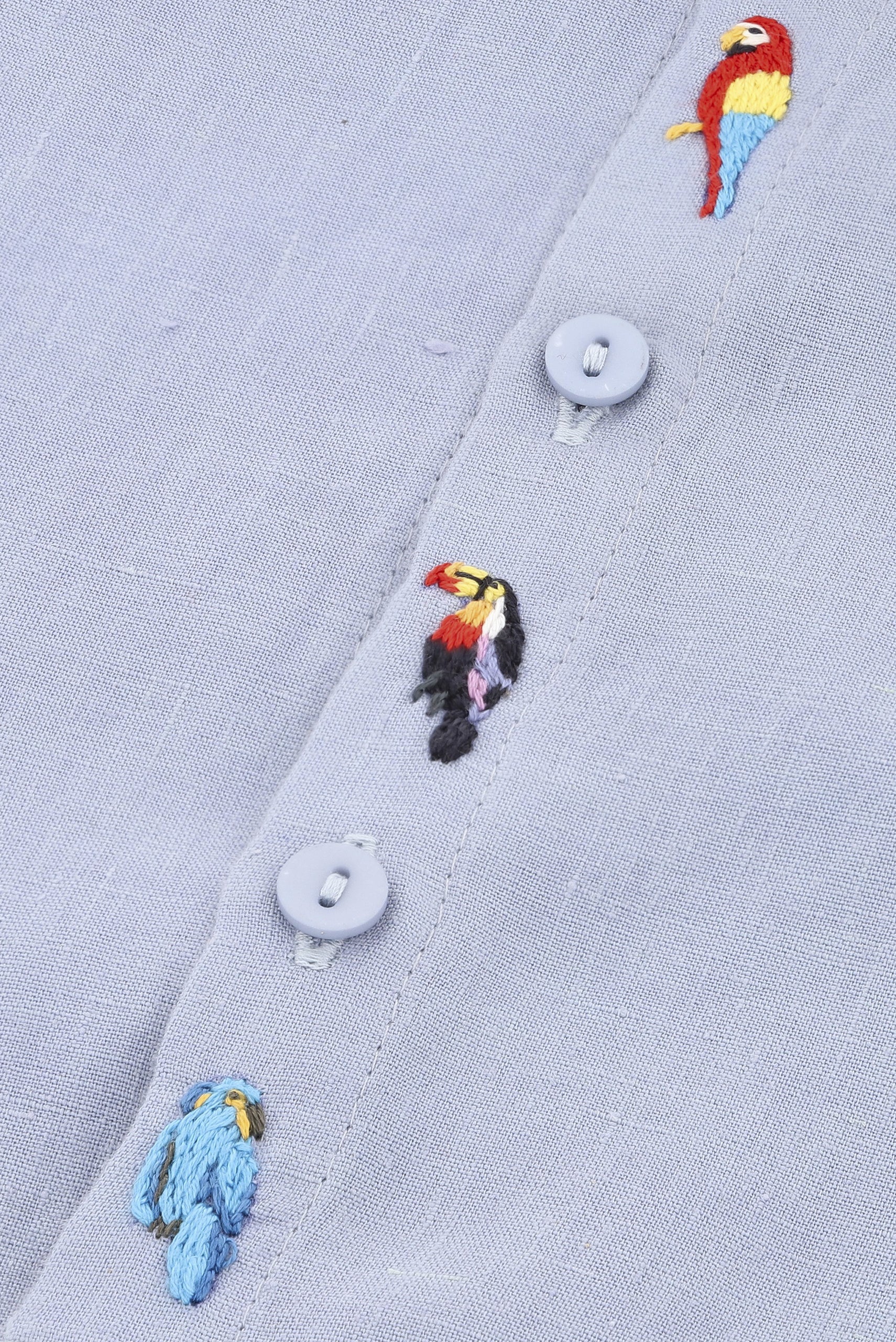 Detalhe dos bordados à mão de tucano e arara em macaquinho infantil de linho azul claro