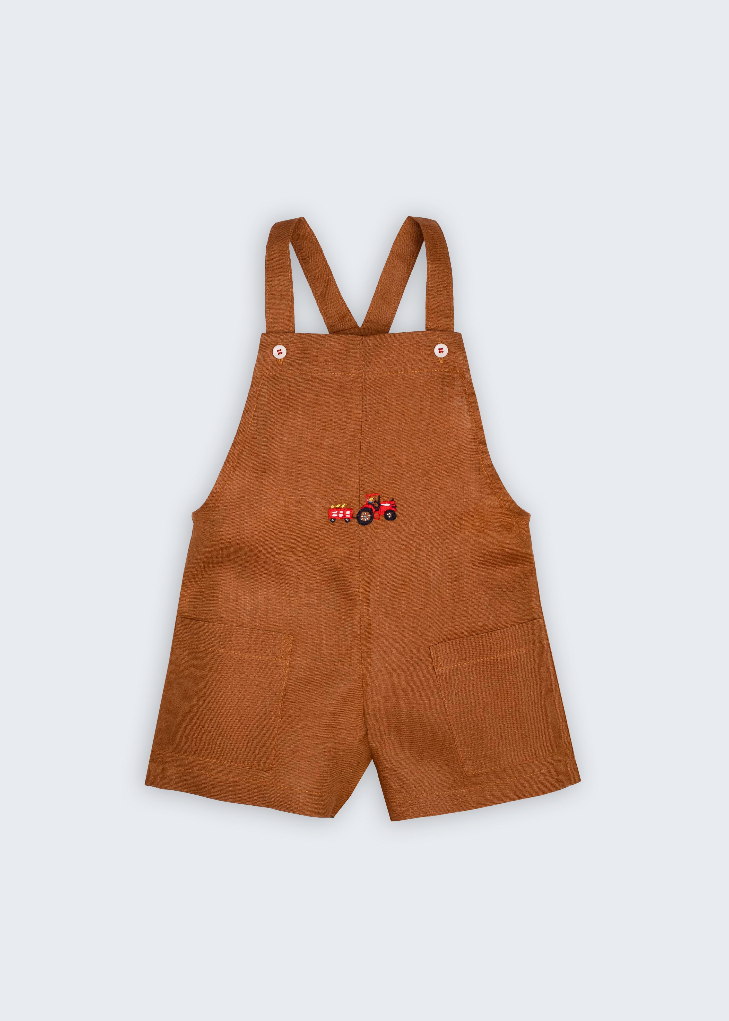 Macaquinho Jardineira Sol infantil em 100% linho caramelo fotografado de frente, com alças de botão, bolsos e bordado de trator.