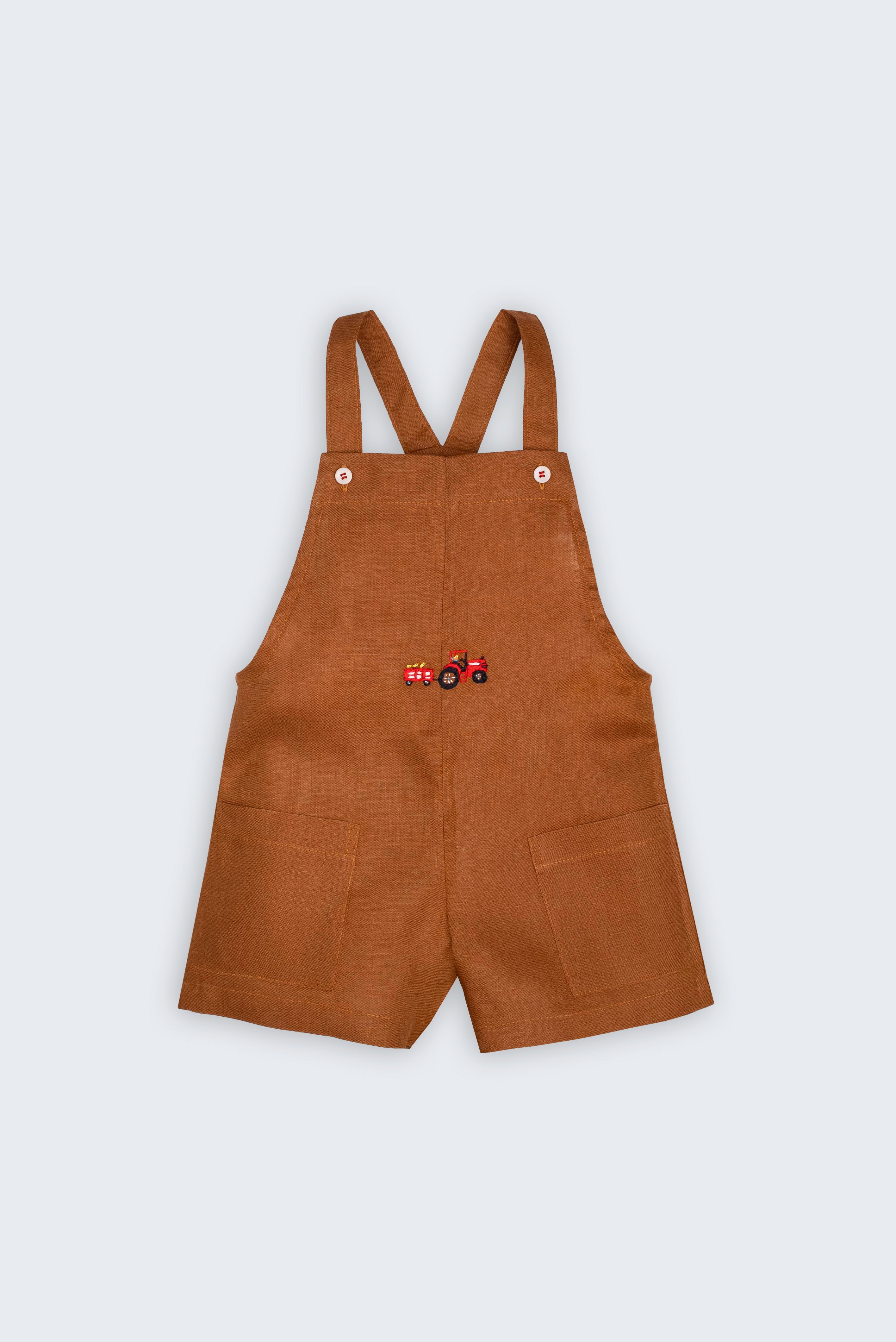 Macaquinho Jardineira Sol infantil em 100% linho caramelo fotografado de frente, com alças de botão, bolsos e bordado de trator.