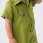 Detalhe do Macaquinho Tiê em linho verde vestido, mostrando bordado artesanal de onça entre folhas.