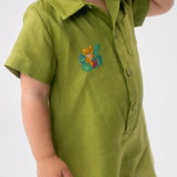 Detalhe do Macaquinho Tiê em linho verde vestido, mostrando bordado artesanal de onça entre folhas.