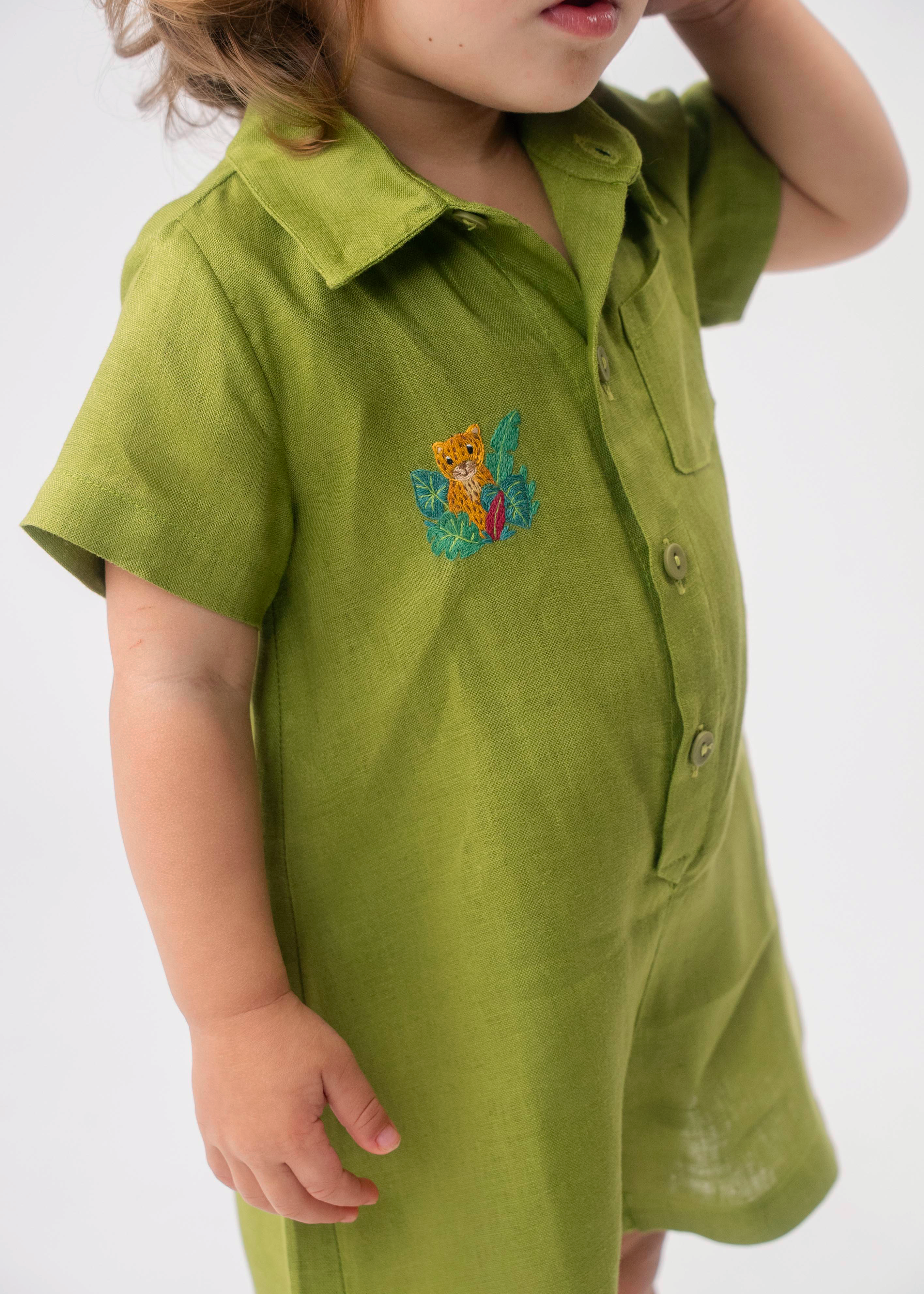 Detalhe do Macaquinho Tiê em linho verde vestido, mostrando bordado artesanal de onça entre folhas.