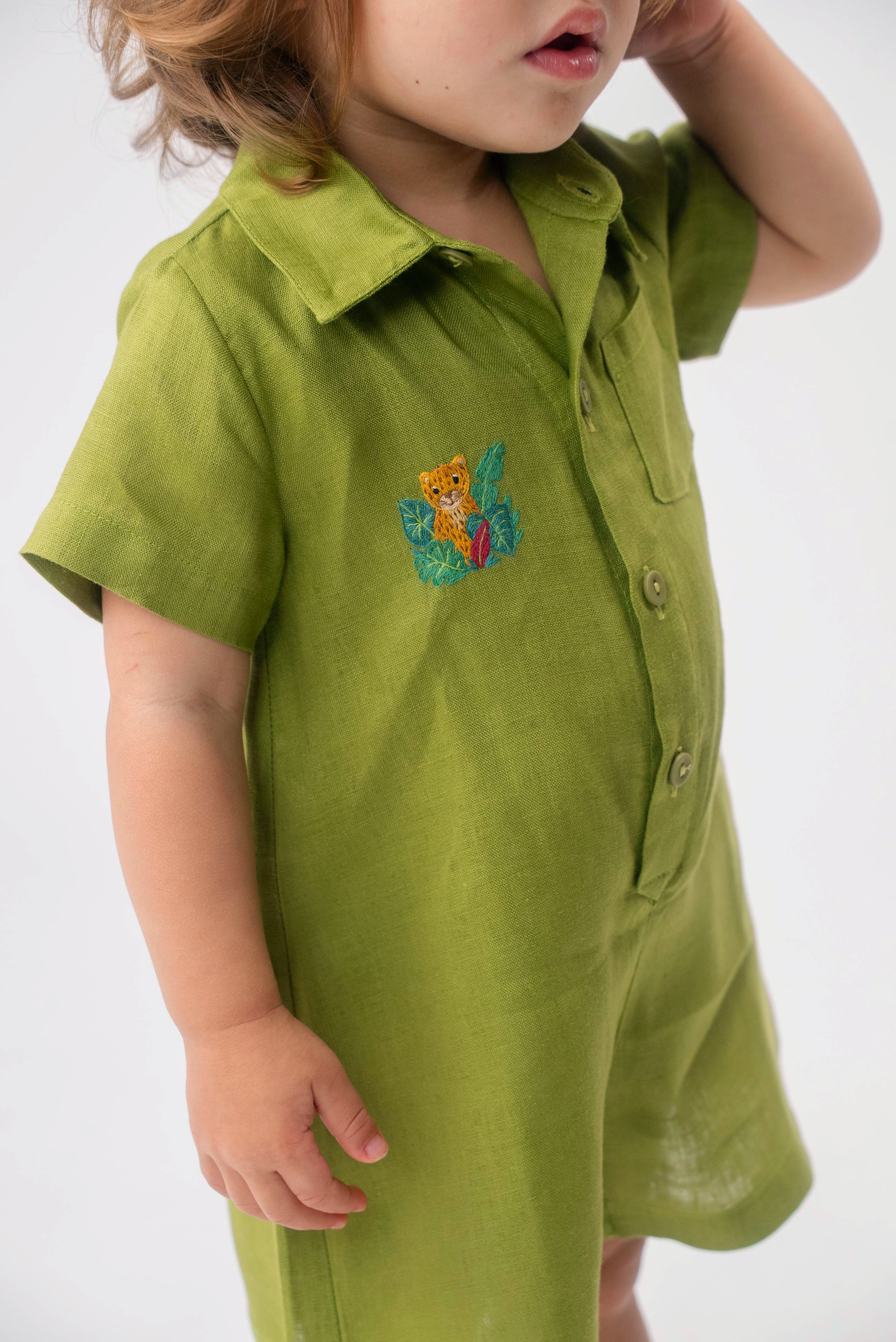 Detalhe do Macaquinho Tiê em linho verde vestido, mostrando bordado artesanal de onça entre folhas.