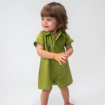 Criança usando Macaquinho Tiê infantil em linho verde com gola, mangas curtas e bordado de onça à mão.