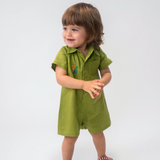 Criança usando Macaquinho Tiê infantil em linho verde com gola, mangas curtas e bordado de onça à mão.